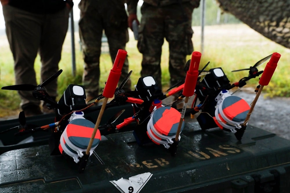 Three first-person-view quadcopters with training payloads line up on a transport case.