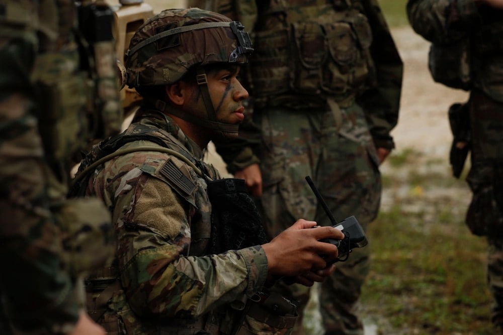 A soldier works a handheld drone controller in the rain as others wait behind.