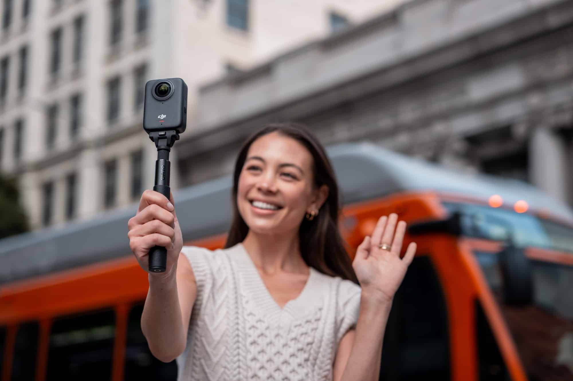 Vlogger waves while holding a 360 camera on an invisible selfie stick.