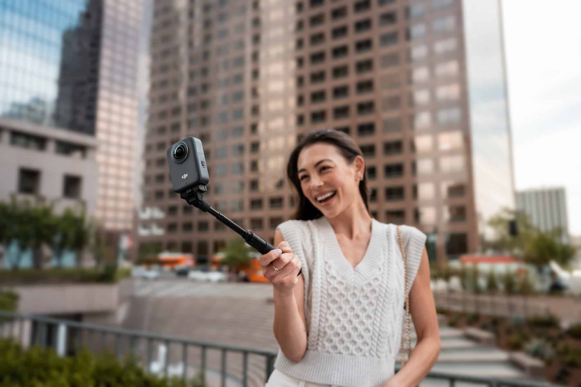 A woman gestures toward the camera raised over a plaza ringed by downtown high-rises.