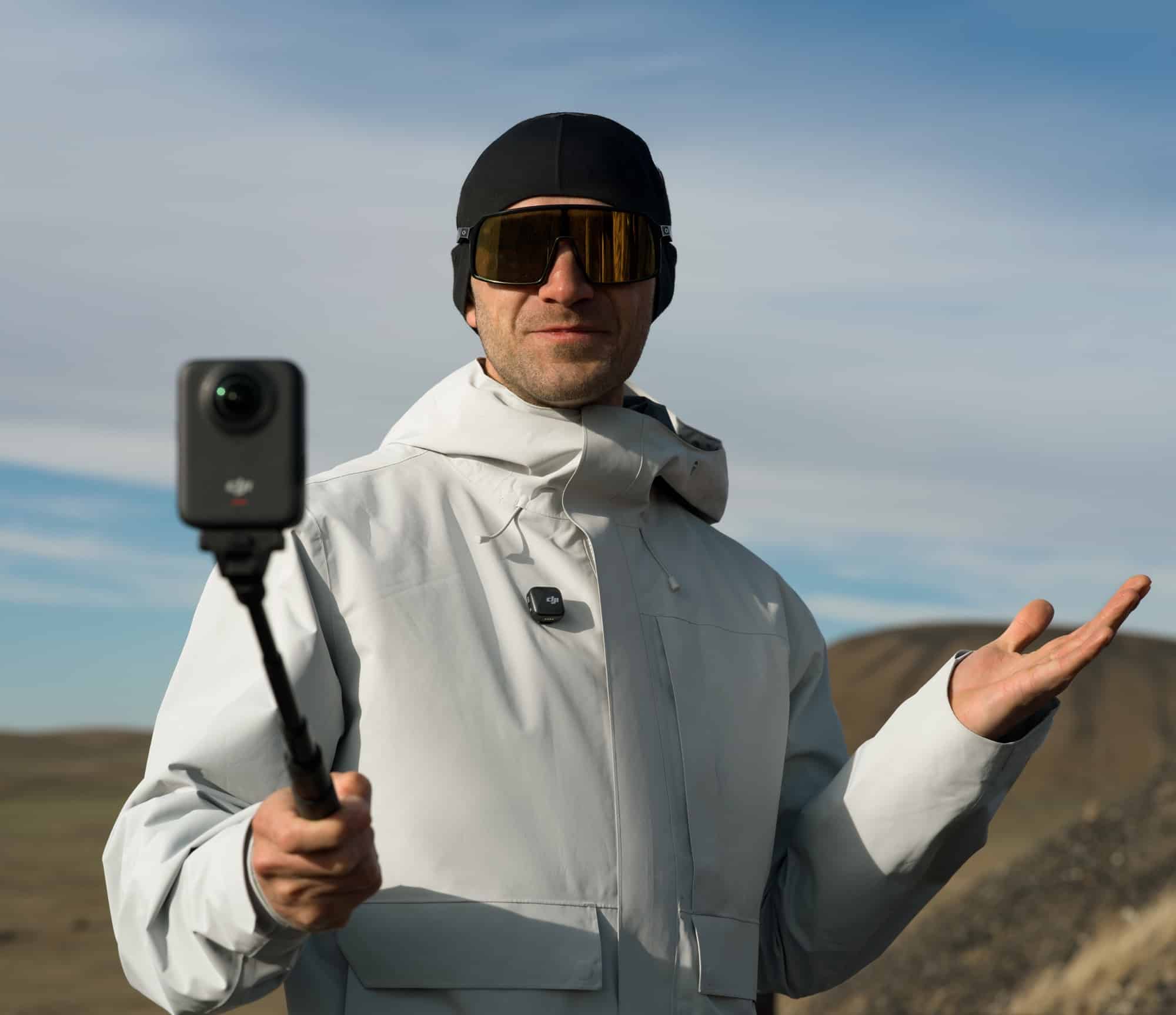 A hiker in a beanie holds the camera aloft with a microphone clipped to his jacket.