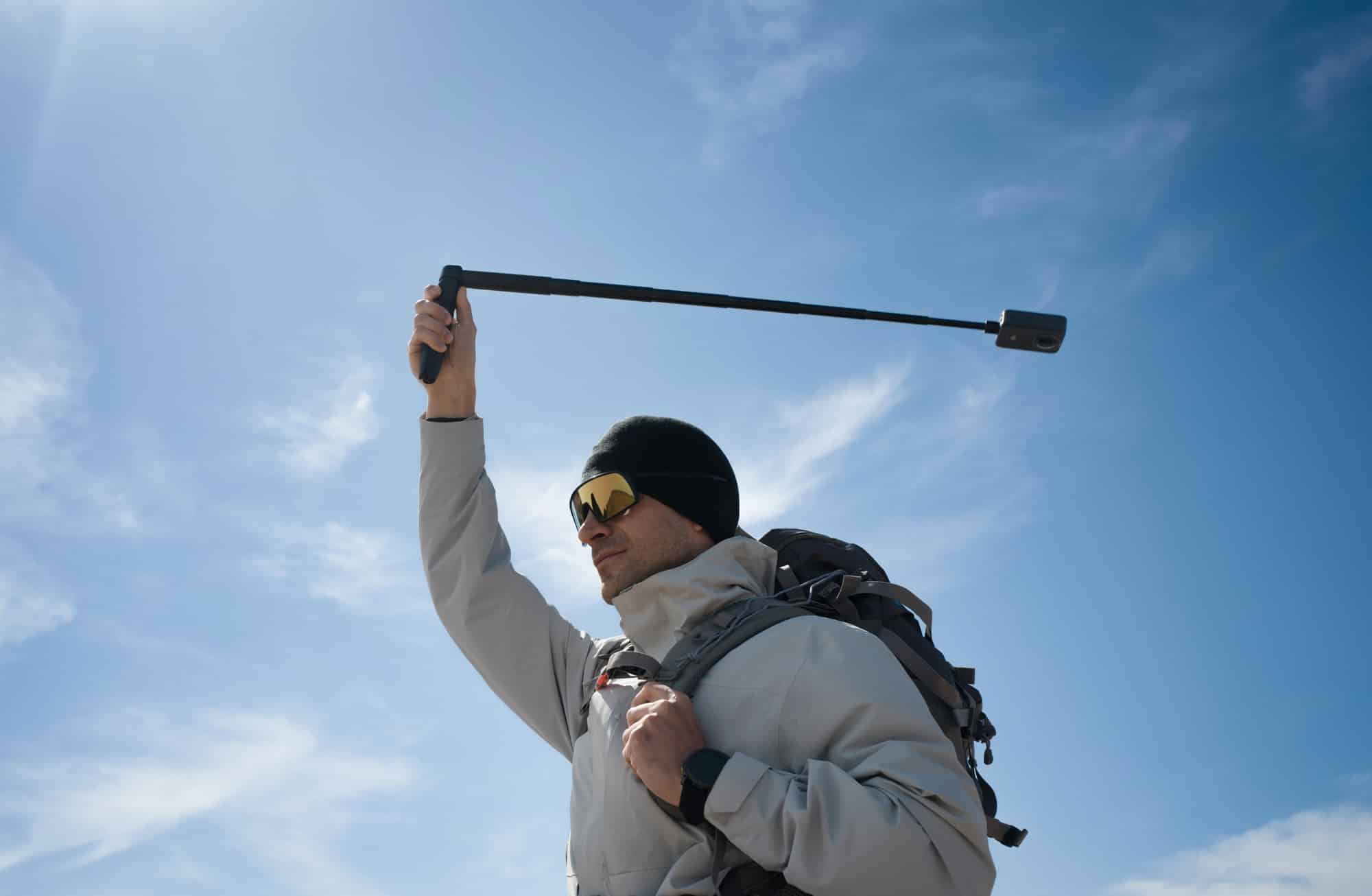 A hiker in sunglasses lifts the camera overhead on a rotating handle.