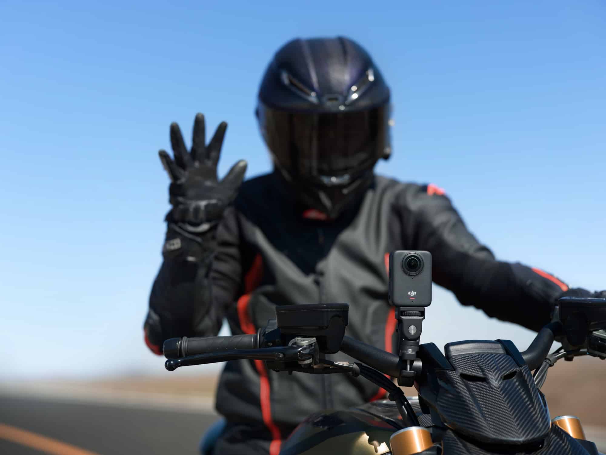 A gloved rider raises an open palm at the handlebar camera to trigger gesture control.