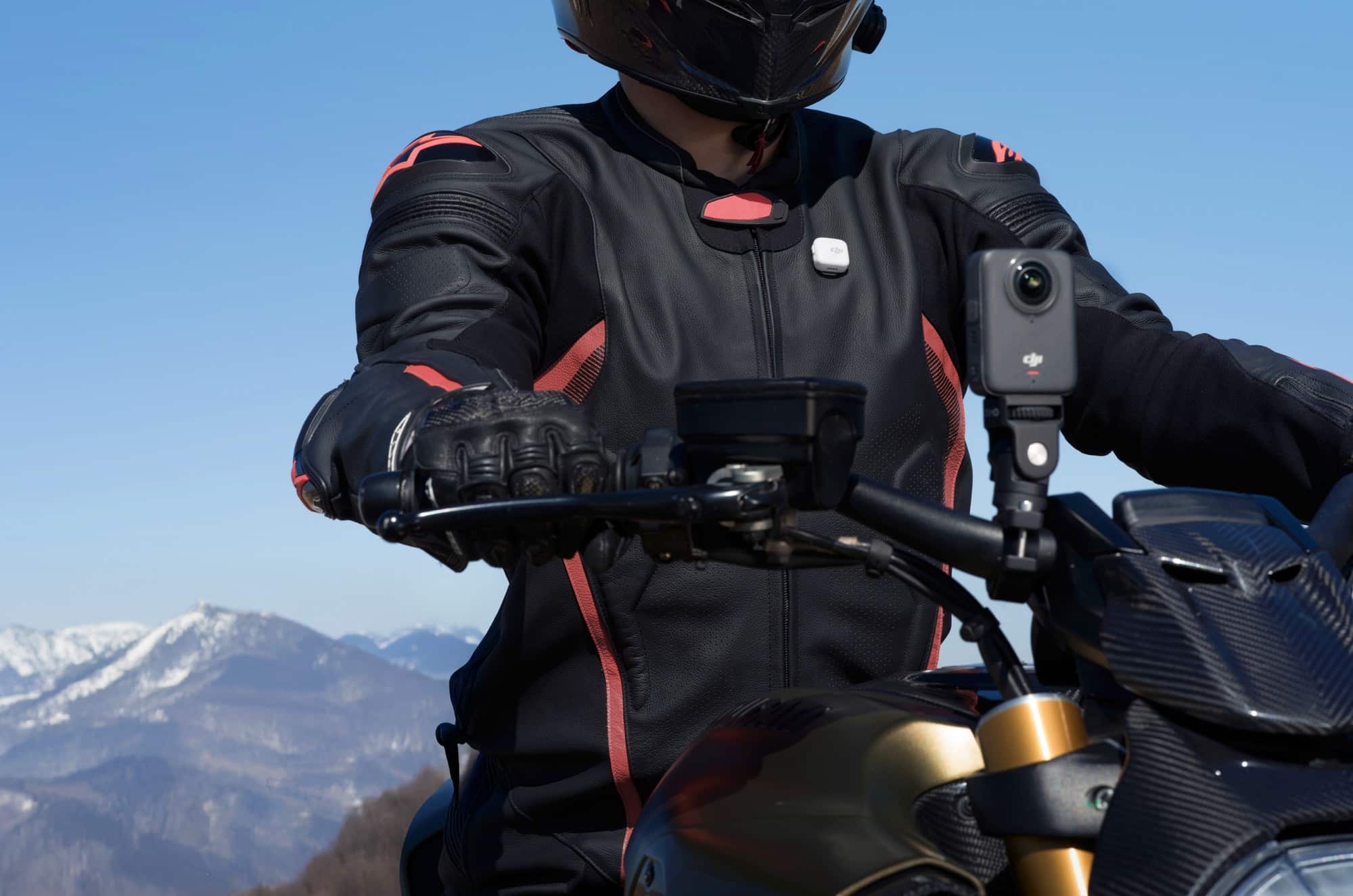 A rider wears a clip-on wireless microphone with mountains beyond the handlebars.