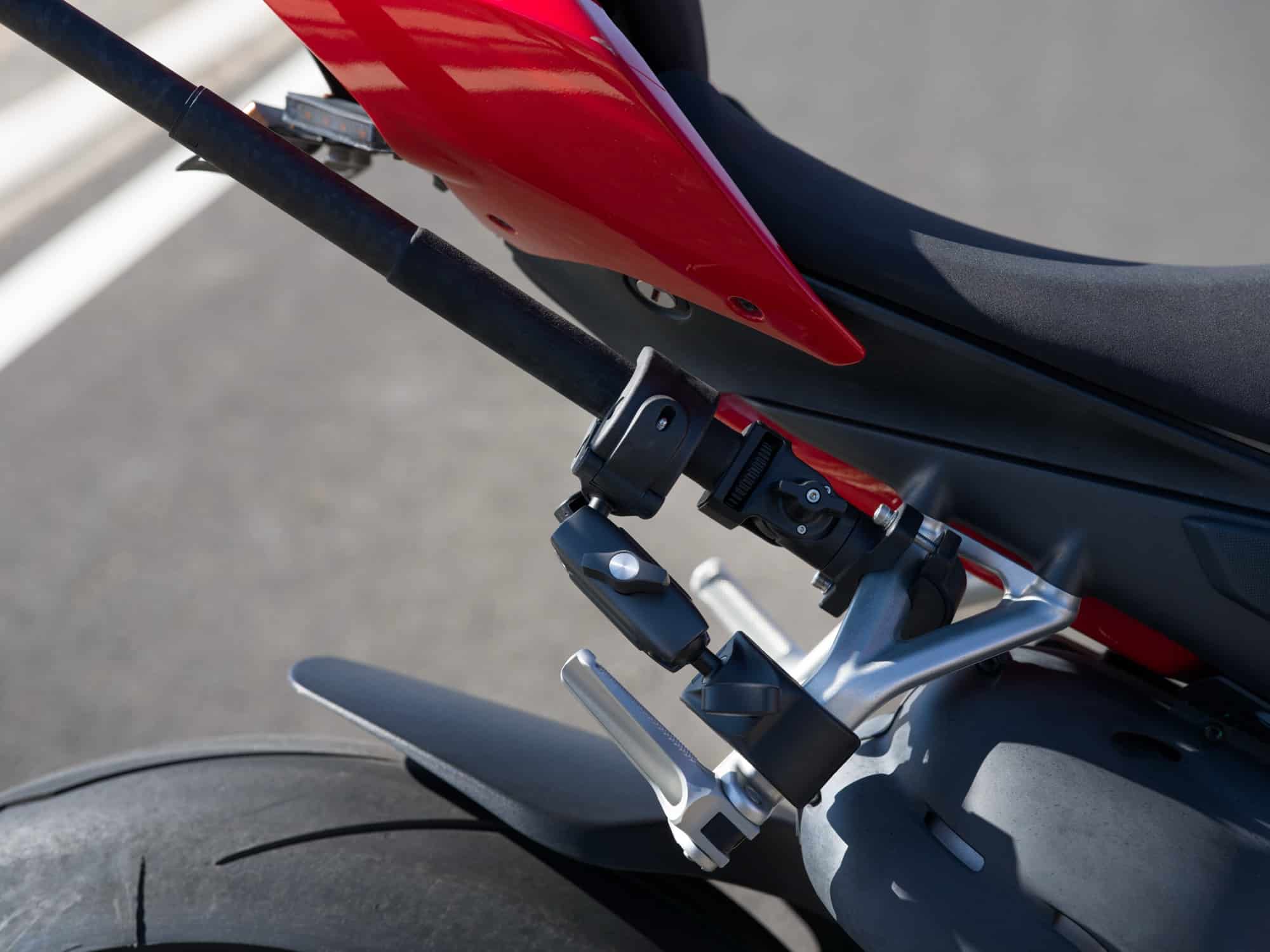 Close-up of a dual heavy-duty clamp holding the camera beside a red motorcycle tail.
