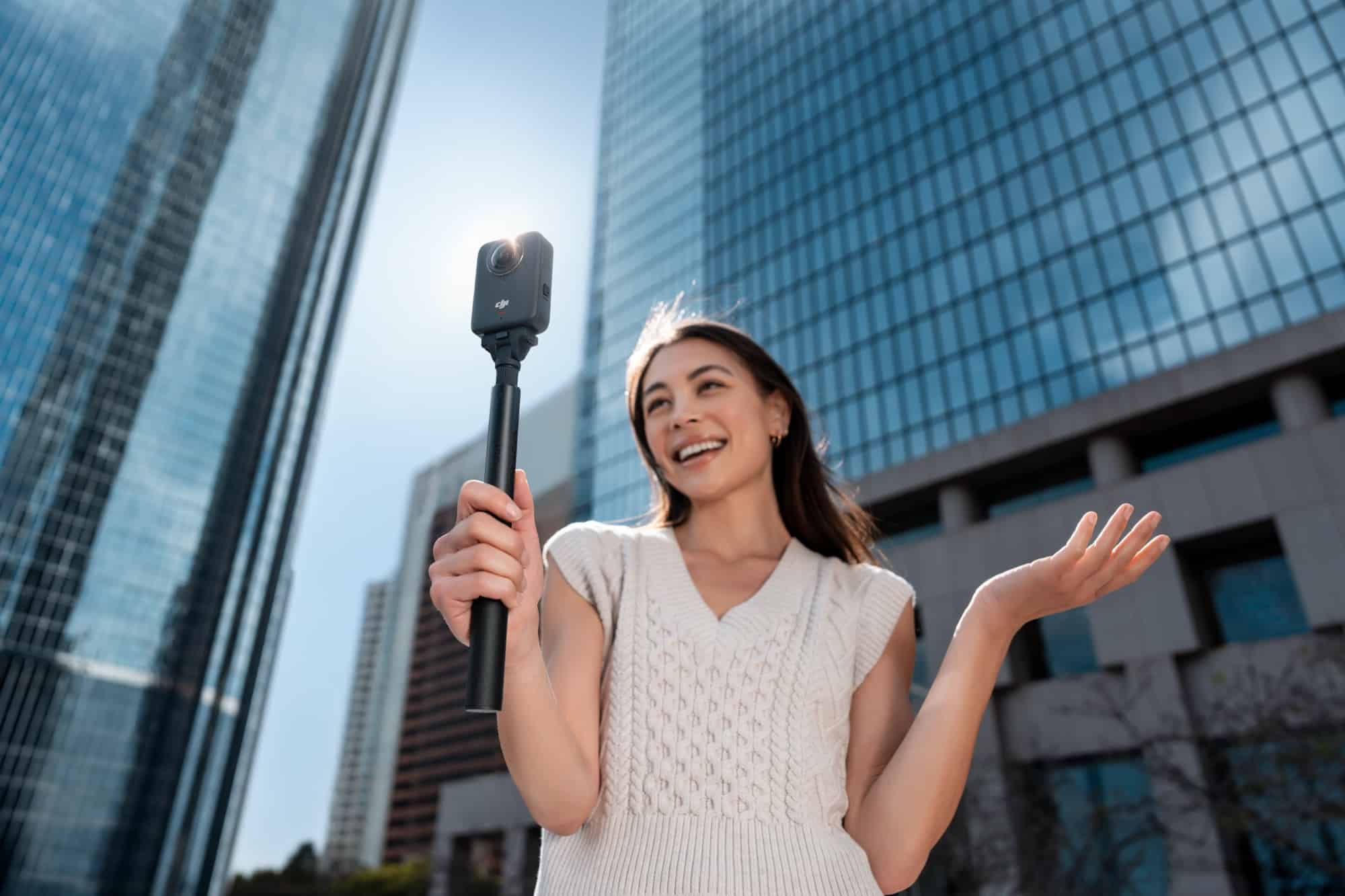 A creator raises the Osmo 360 on a selfie stick between mirrored office towers.