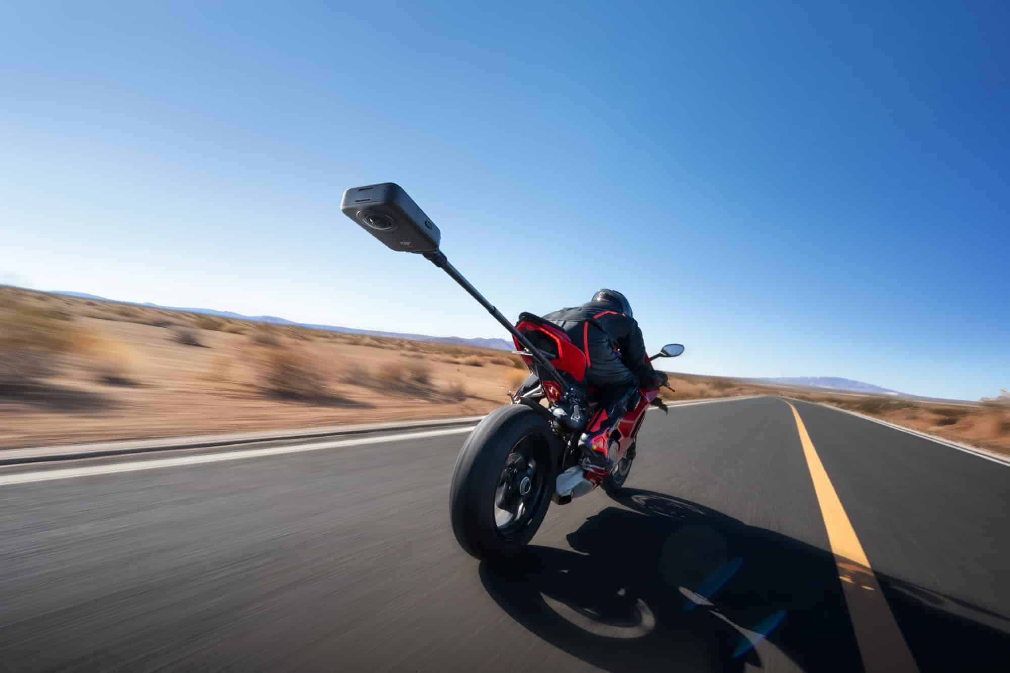 A red motorcycle banks through a desert highway curve trailed by the camera boom.