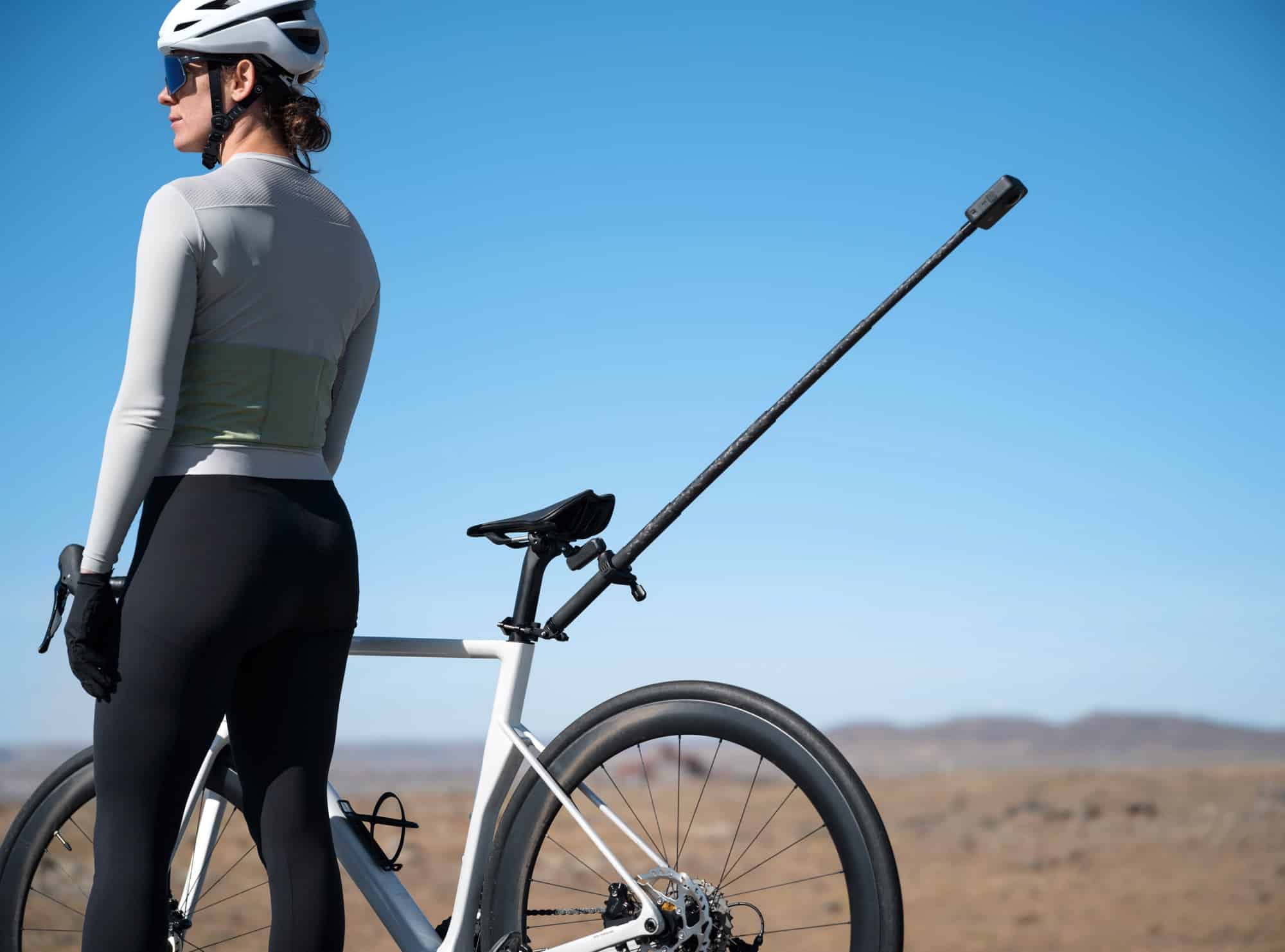 A cyclist stands beside a road bike with the camera rod mounted behind the saddle.