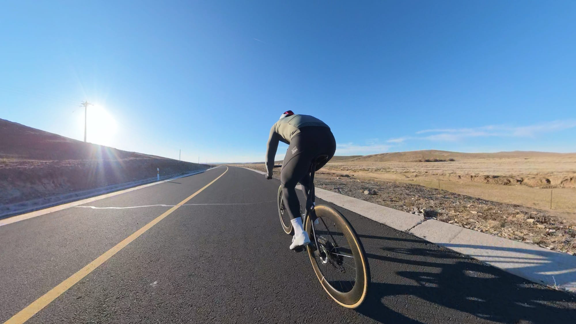 Wide 360 view of a cyclist sprinting along a sunlit rural highway.