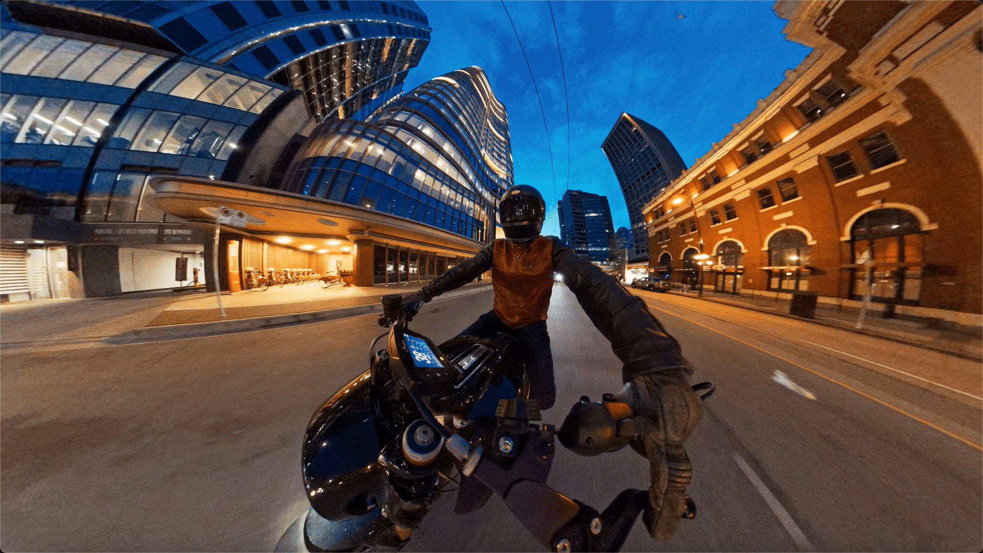 Fisheye 360 frame of a motorcyclist leaning through a curved city street.