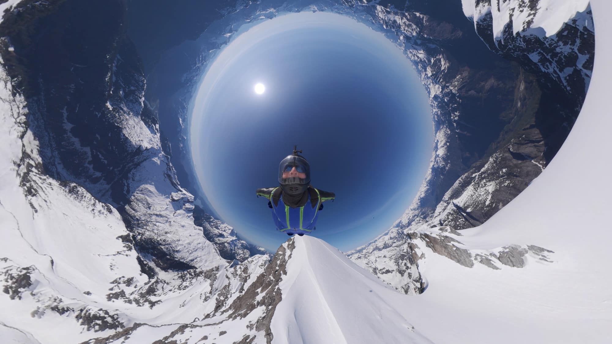 Fisheye 360 view of a rider on a snow ridge with mountains bending overhead.