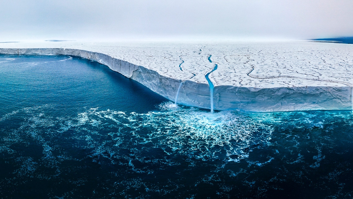 Aerial of an ice shelf edge meeting turquoise meltwater.