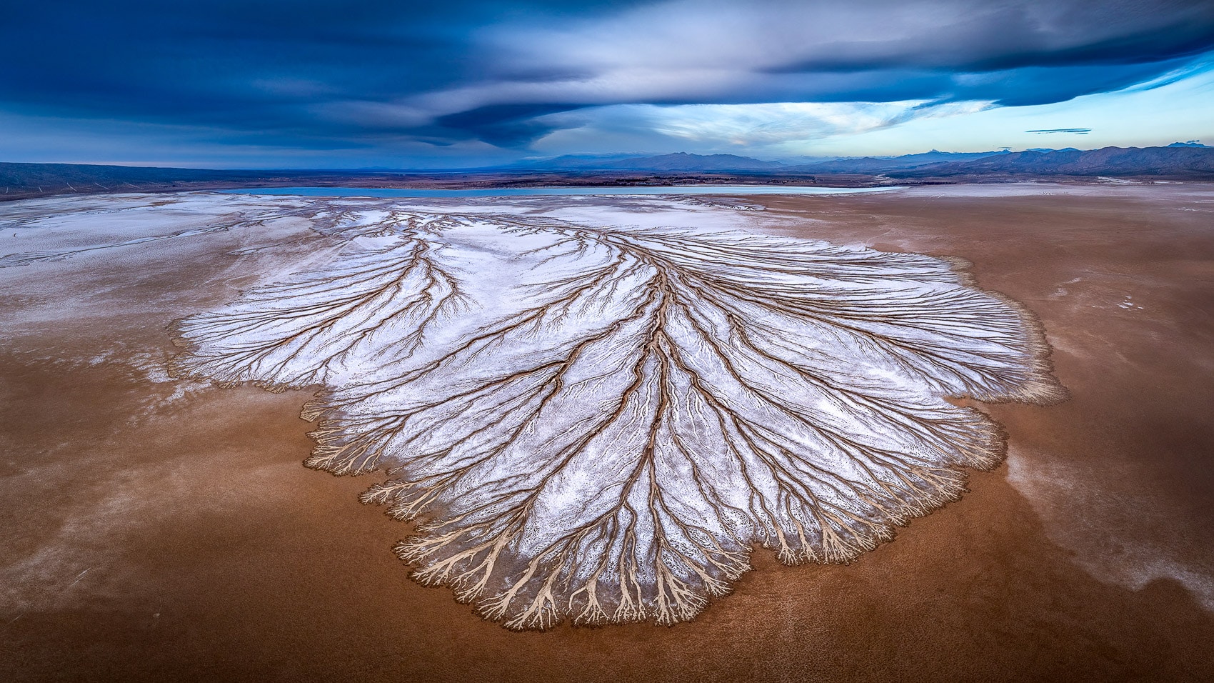 White fan-shaped salt delta spreading across rust-colored ground from above.
