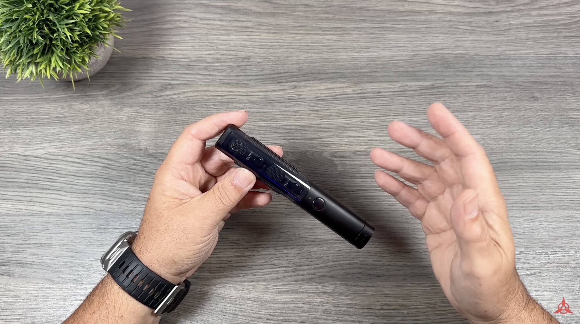 Hands holding the slim black Boya Magic wireless microphone above a wooden desk.