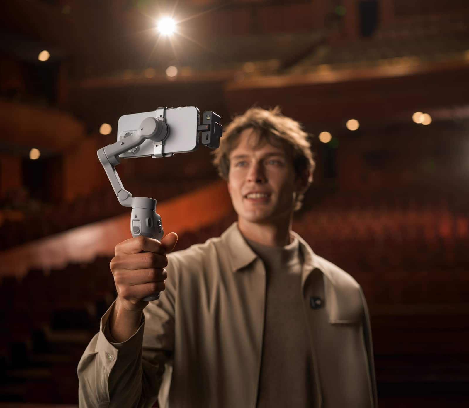 Man films himself with a phone on a gimbal inside a theater auditorium.