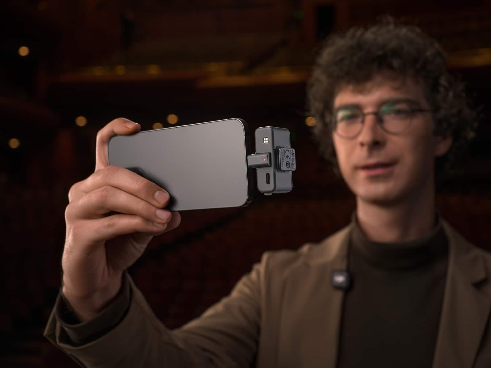 Man in glasses holds a phone with the receiver clipped to its side.