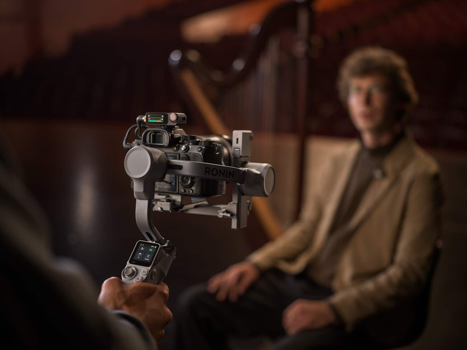 Operator films a seated man using a mirrorless camera on a compact gimbal.