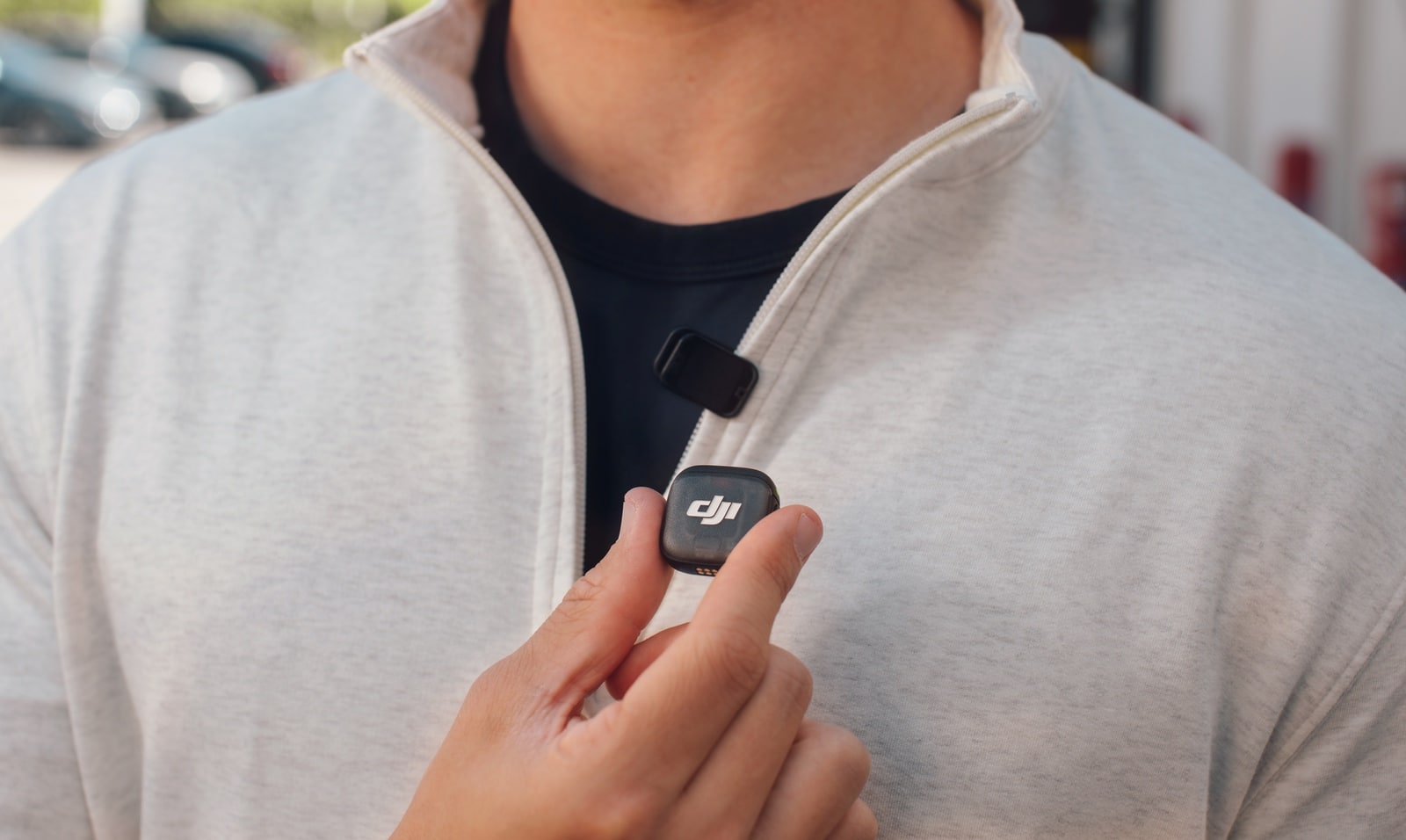 Hand lifts a magnetic transmitter off the front of a cream jacket.