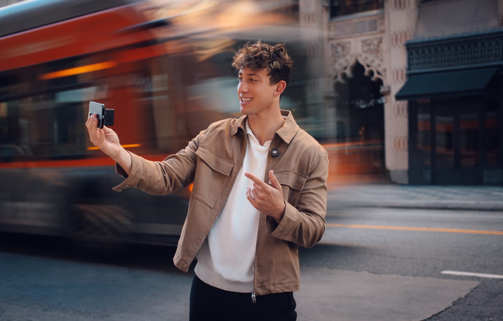 Man gestures on a city street as a red bus blurs past.