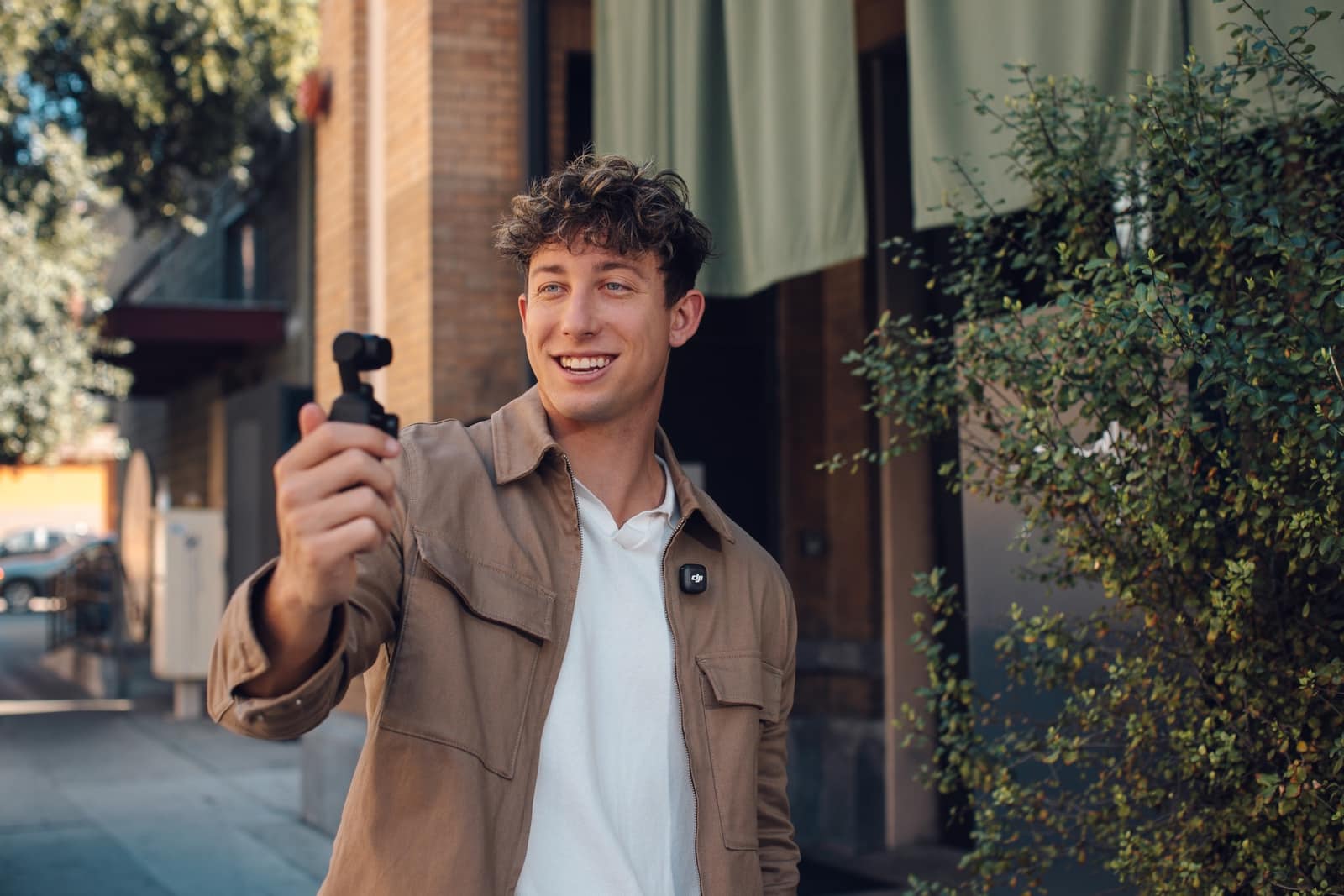 Vlogger holds a pocket gimbal camera outside a plant-draped shopfront.