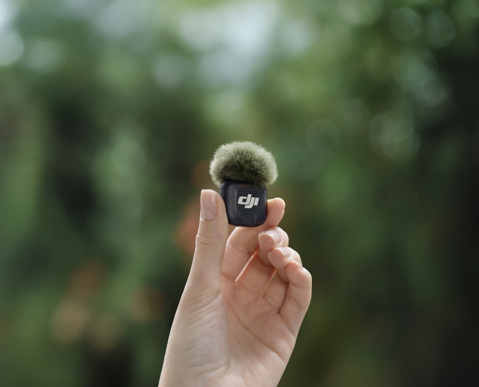 Transmitter capped with a green fur windscreen held against sunlit foliage.