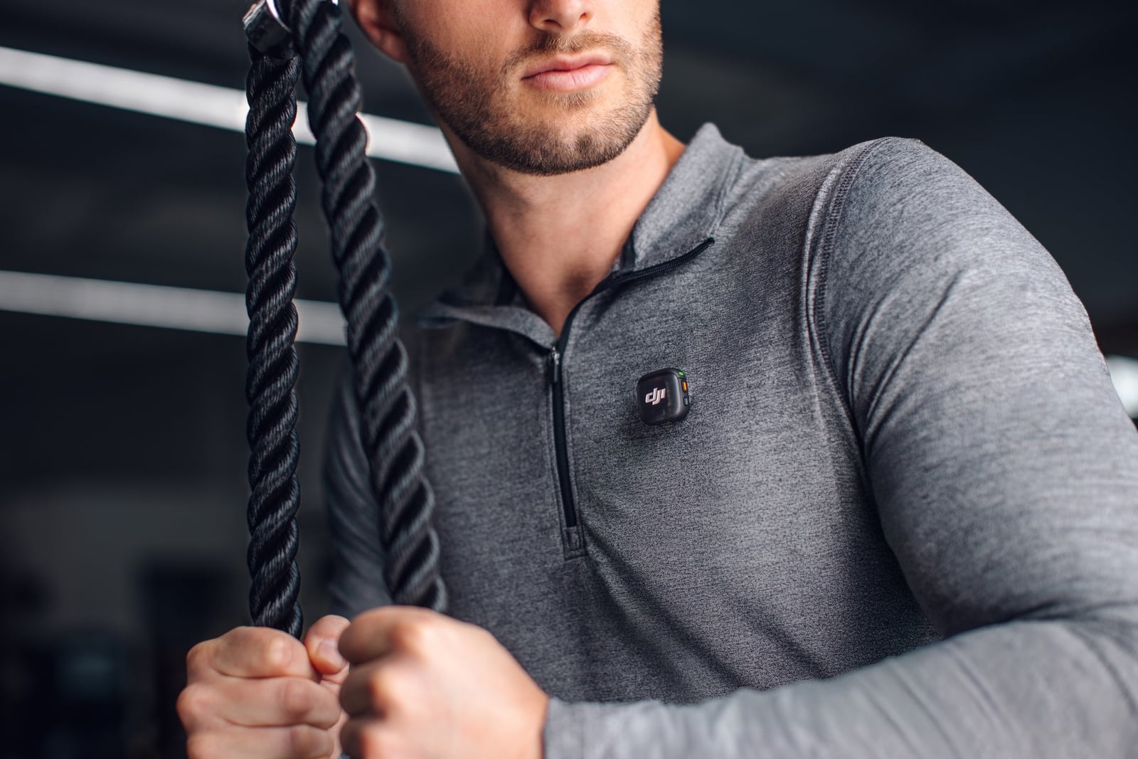 Man in a gray quarter-zip grips battle ropes with a transmitter clipped on.