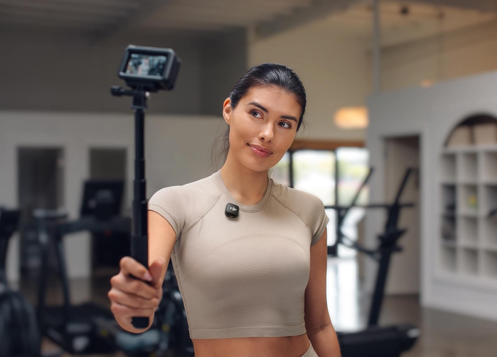 Woman holds an action camera on a stick in a bright gym.