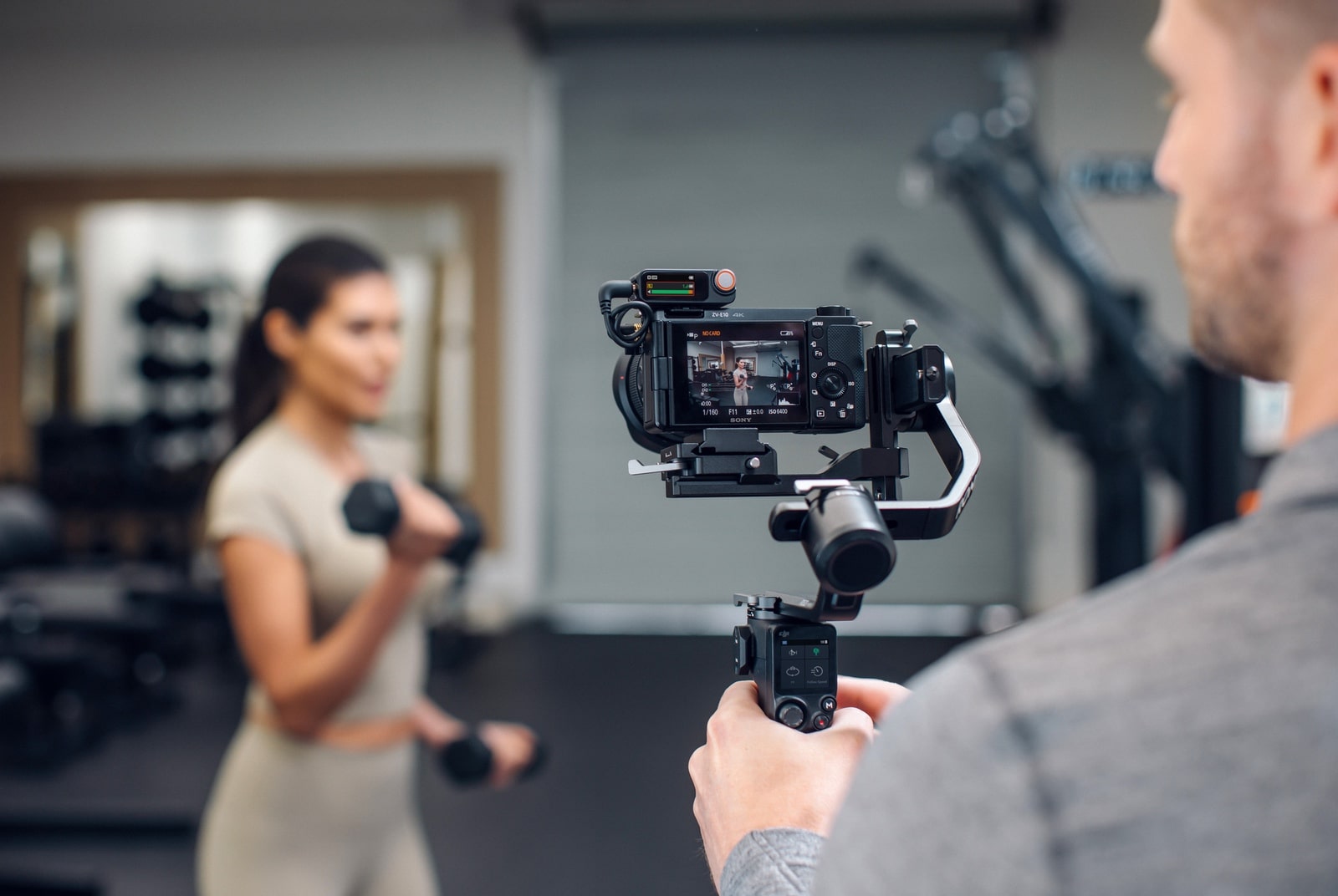 Operator films a woman lifting a dumbbell using a gimbal-mounted camera.