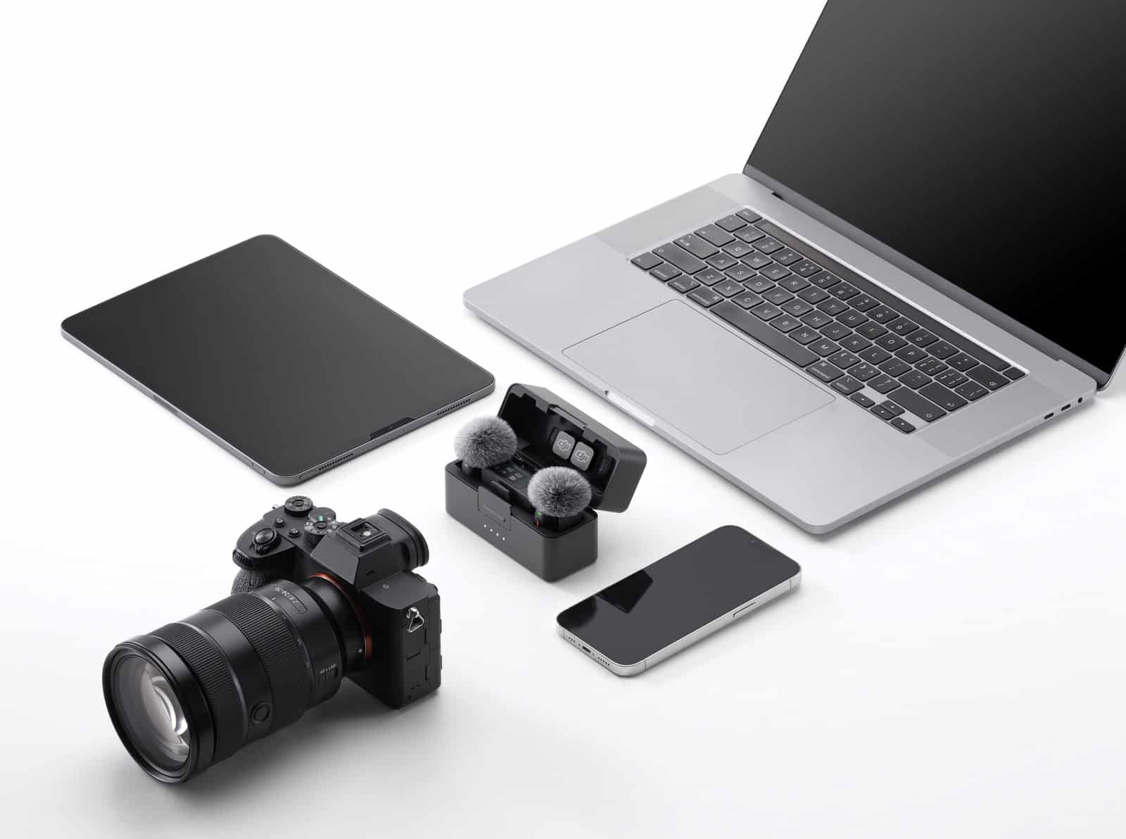 Mirrorless camera, tablet, laptop, phone and open case arranged on white.