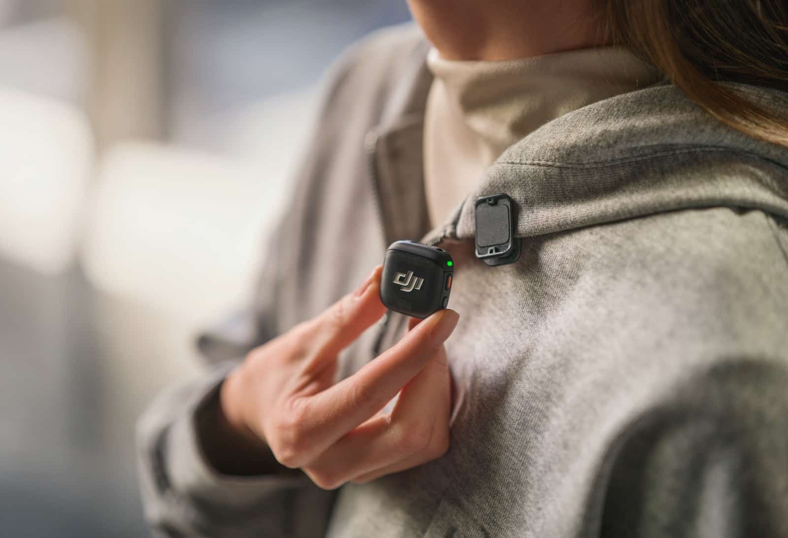 Hand detaches an upside-down transmitter from a beige jacket lapel.