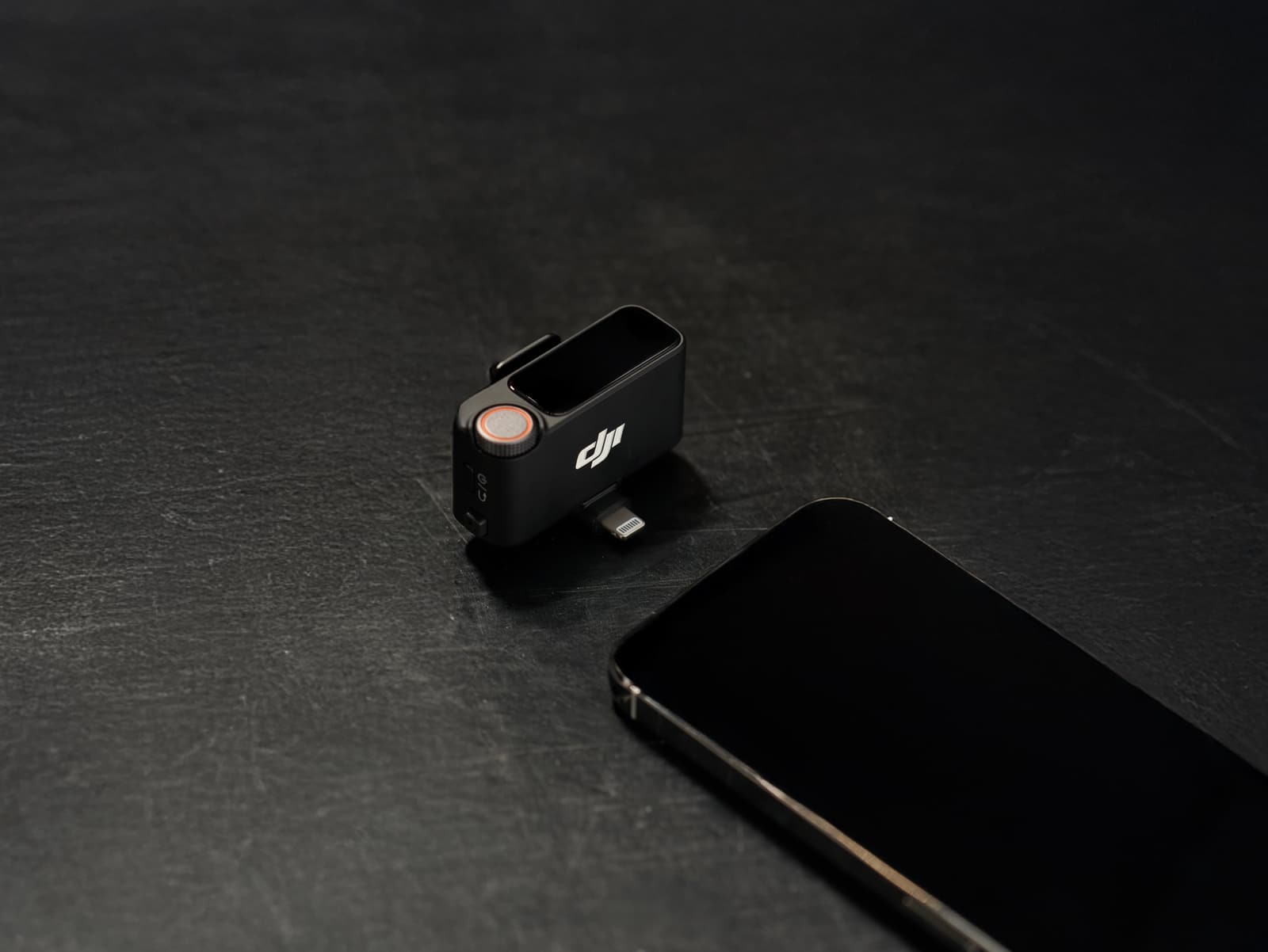 Receiver fitted with a Lightning adapter resting on slate beside a phone.