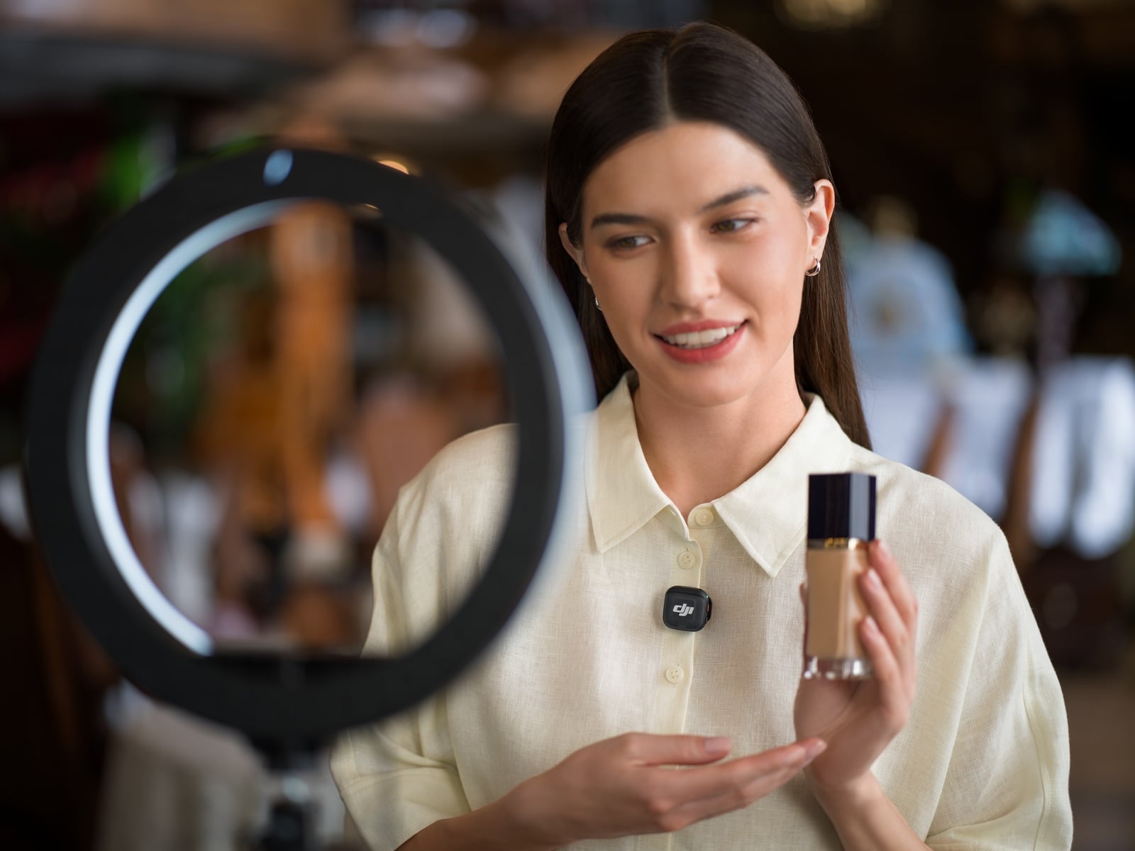 Presenter shows a foundation bottle to a ring light while wearing a transmitter.