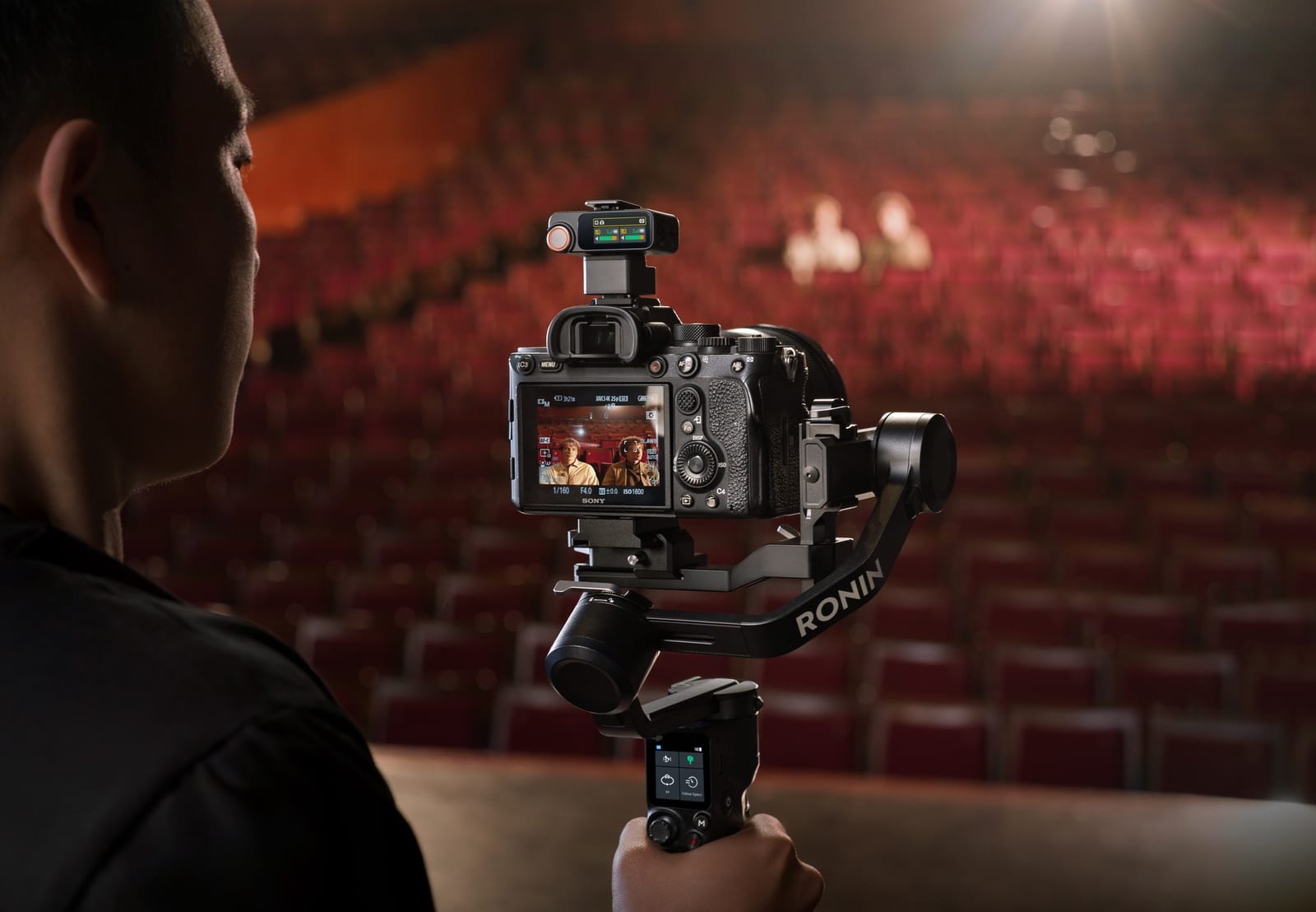 Gimbal camera aims across an empty red-seated auditorium toward a distant subject.