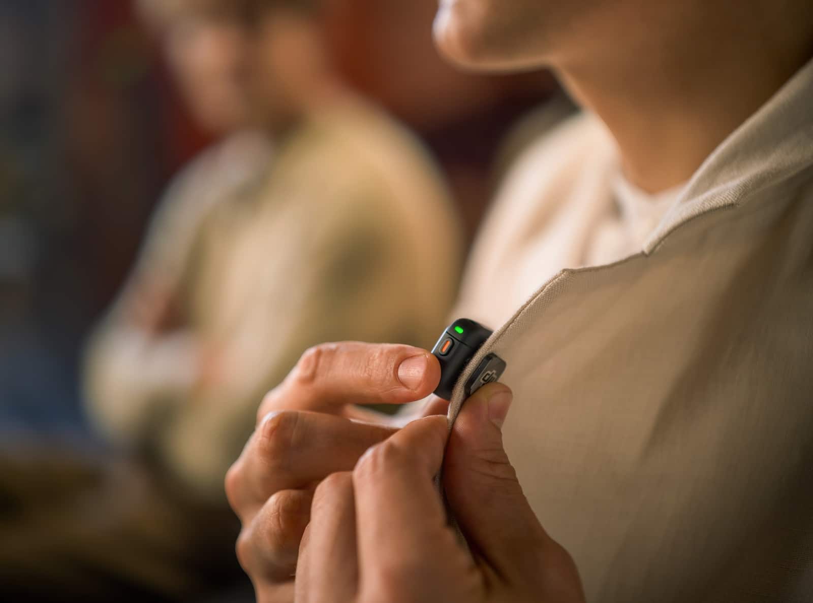 Fingers press the magnetic transmitter onto the front of a beige top.