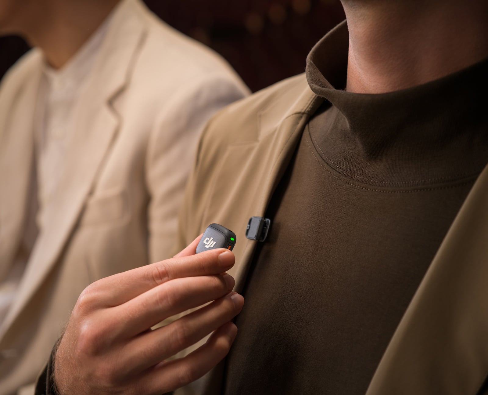 Fingers pull a lit transmitter away from a brown turtleneck collar.