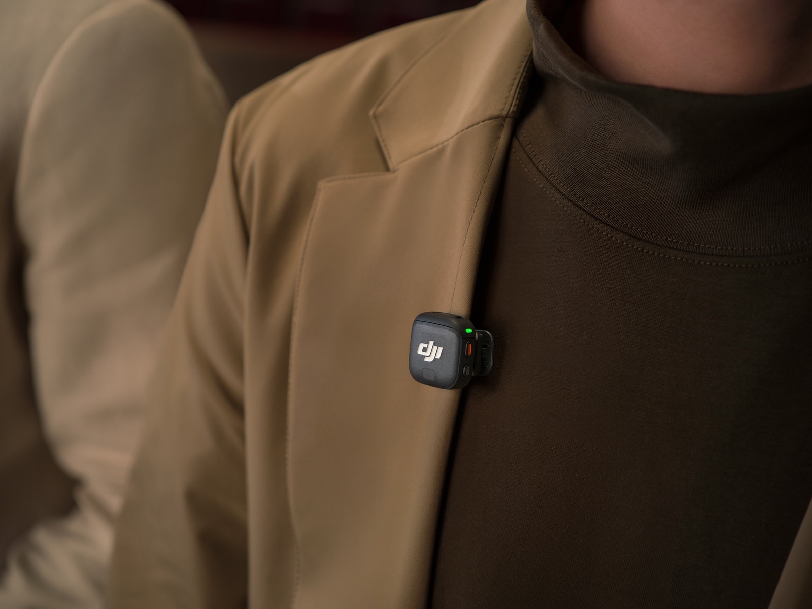 Transmitter clipped to a tan blazer lapel with its green light on.