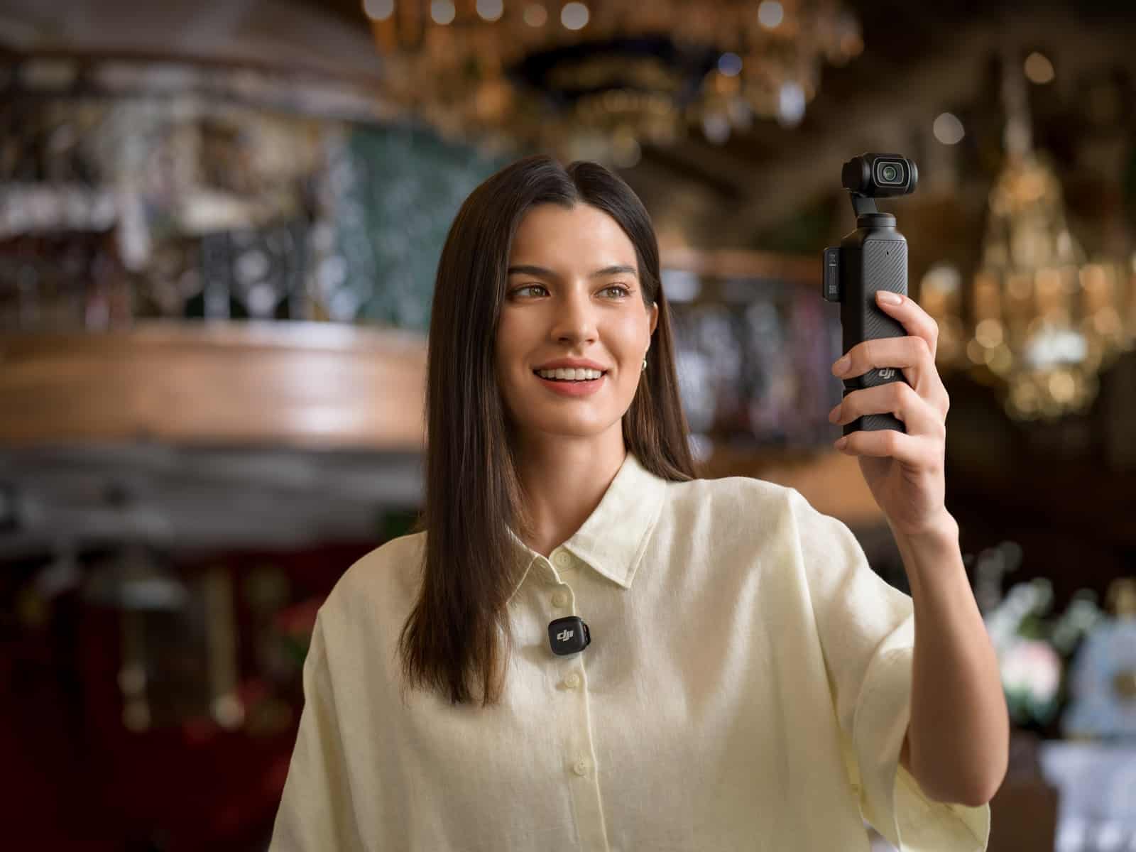 Woman films with a pocket gimbal camera inside an ornate chandelier-lit shop.