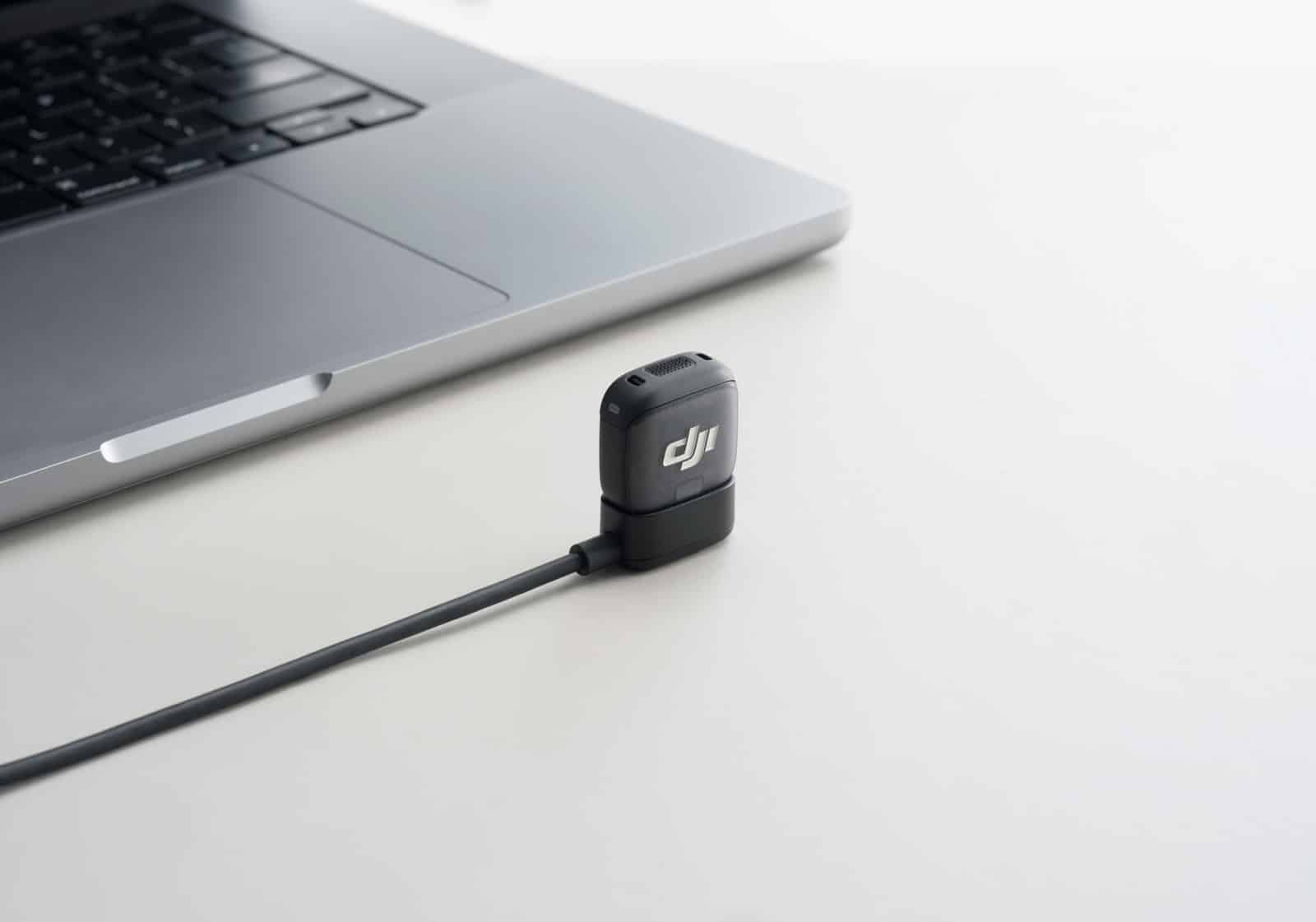 Transmitter on a white desk beside a laptop with its charging cable attached.