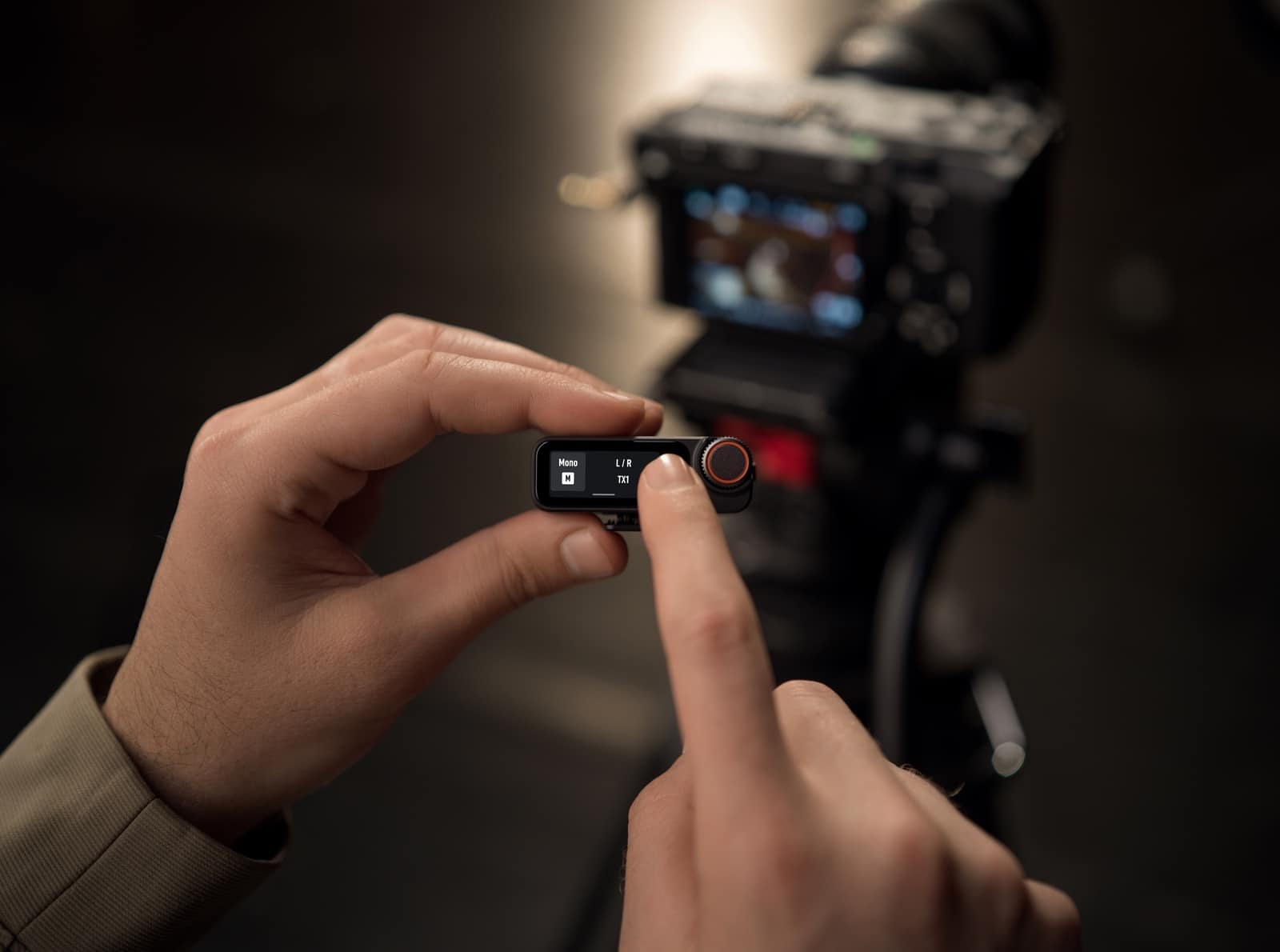 Fingers tap the receiver touchscreen beside a camera rig in low light.