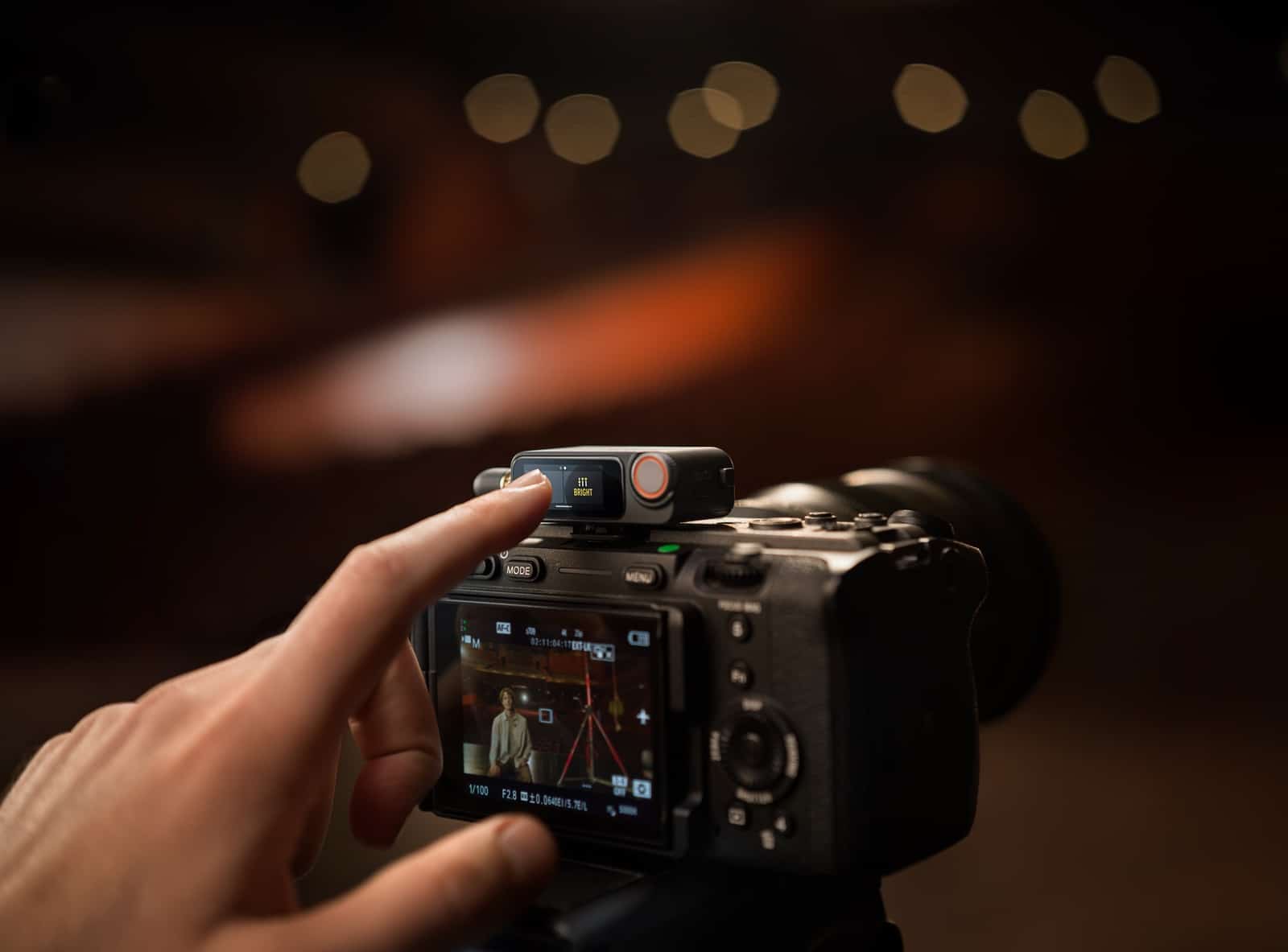Hands adjust the receiver mounted on a mirrorless camera hot shoe.
