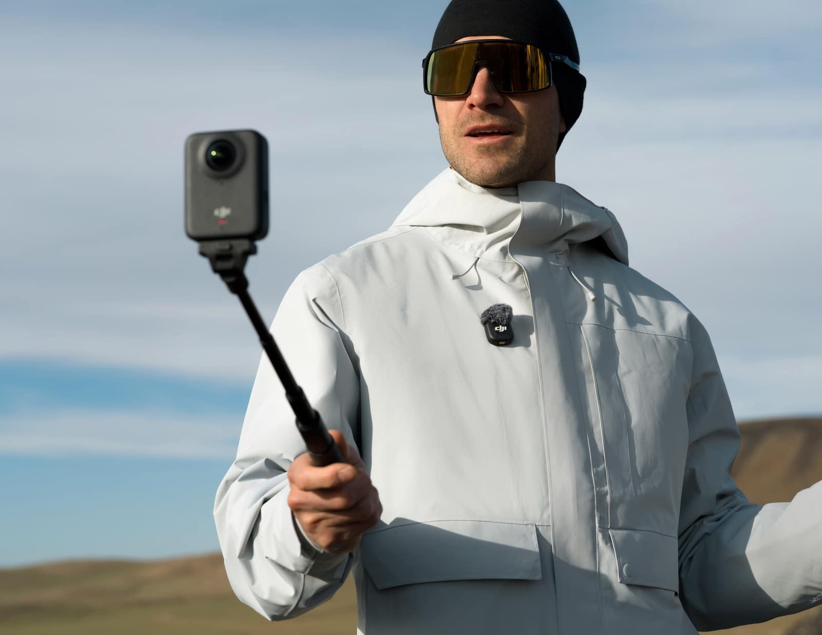 Man in a white hooded jacket raises a 360 camera on a pole.