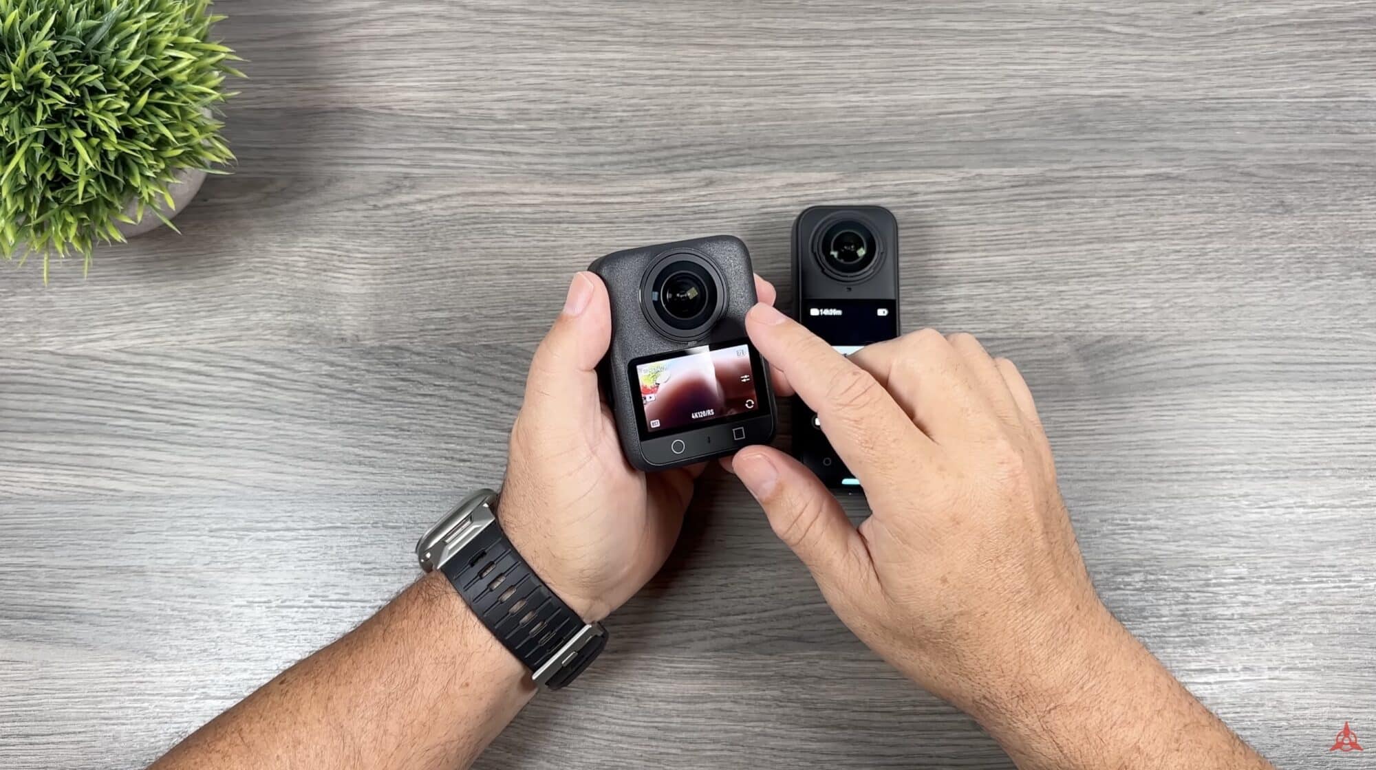 Hands hold the DJI Osmo 360 and Insta360 X5 side by side on a desk.