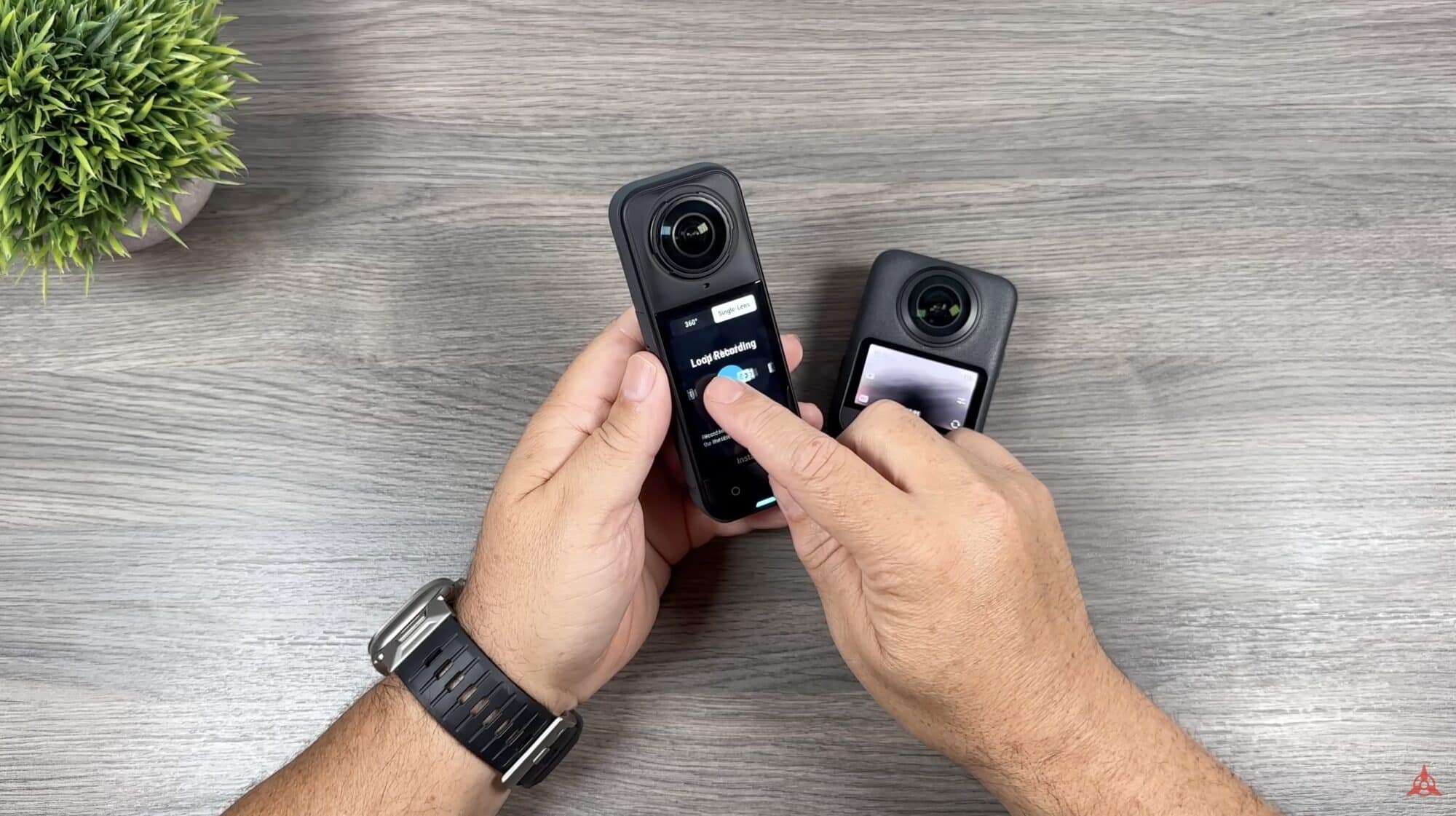 Both 360 cameras stood upright in hand, touchscreens facing the camera.