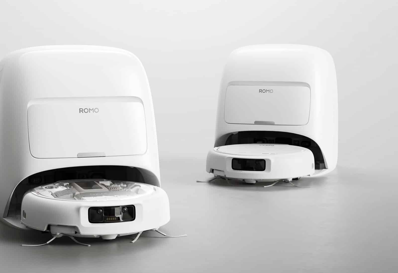 Two white DJI ROMO robot vacuums shown with their docking bases in a studio.
