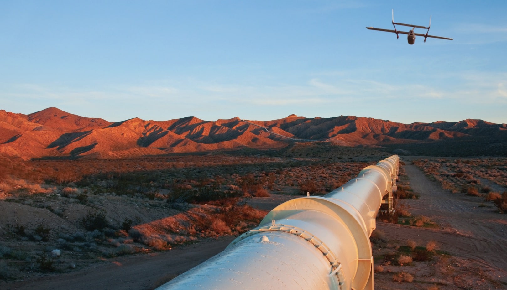 Fixed-wing drone flying a pipeline inspection route across red desert hills.