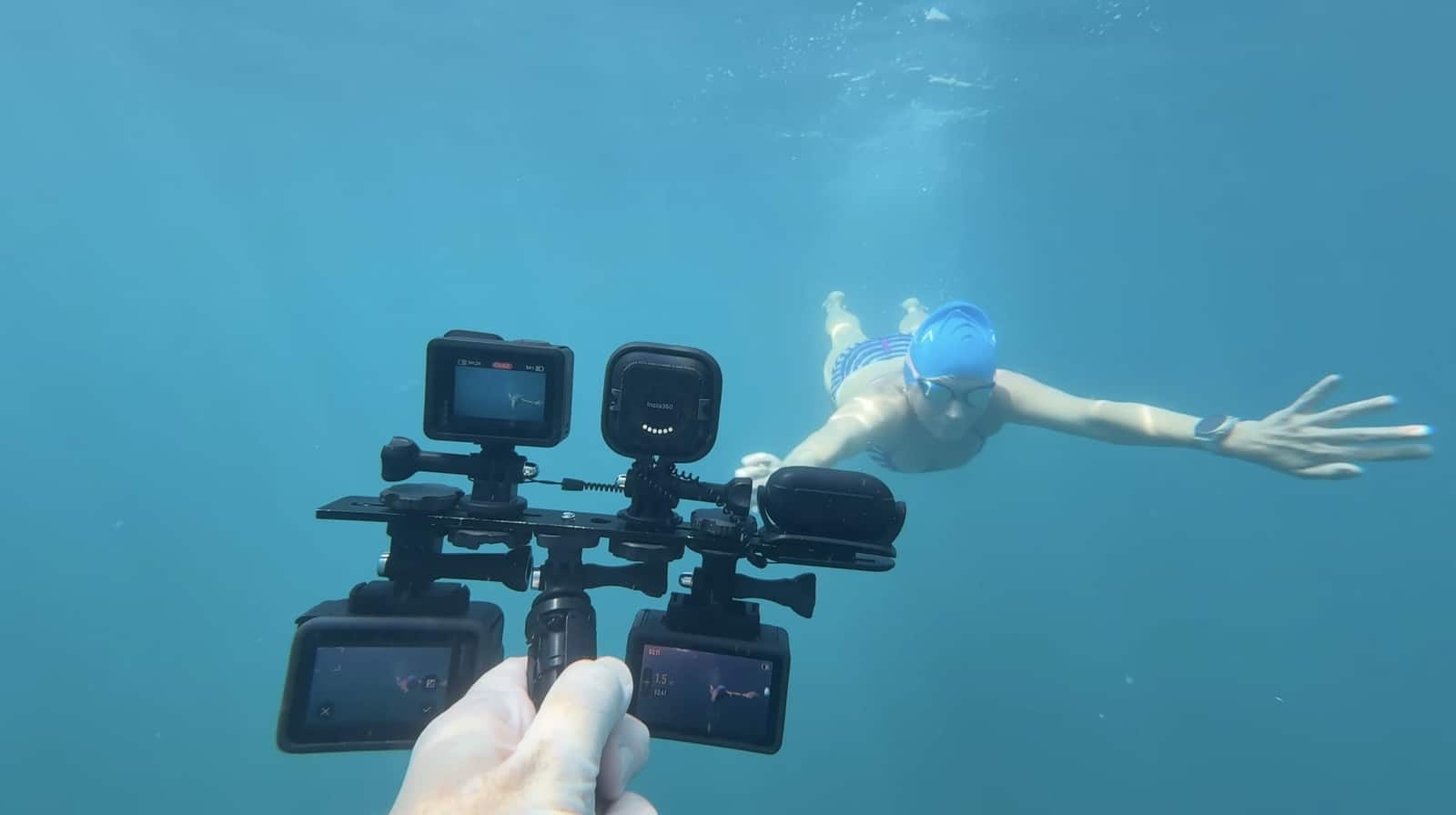 Underwater rig of action cameras filming a snorkeler in clear blue water.