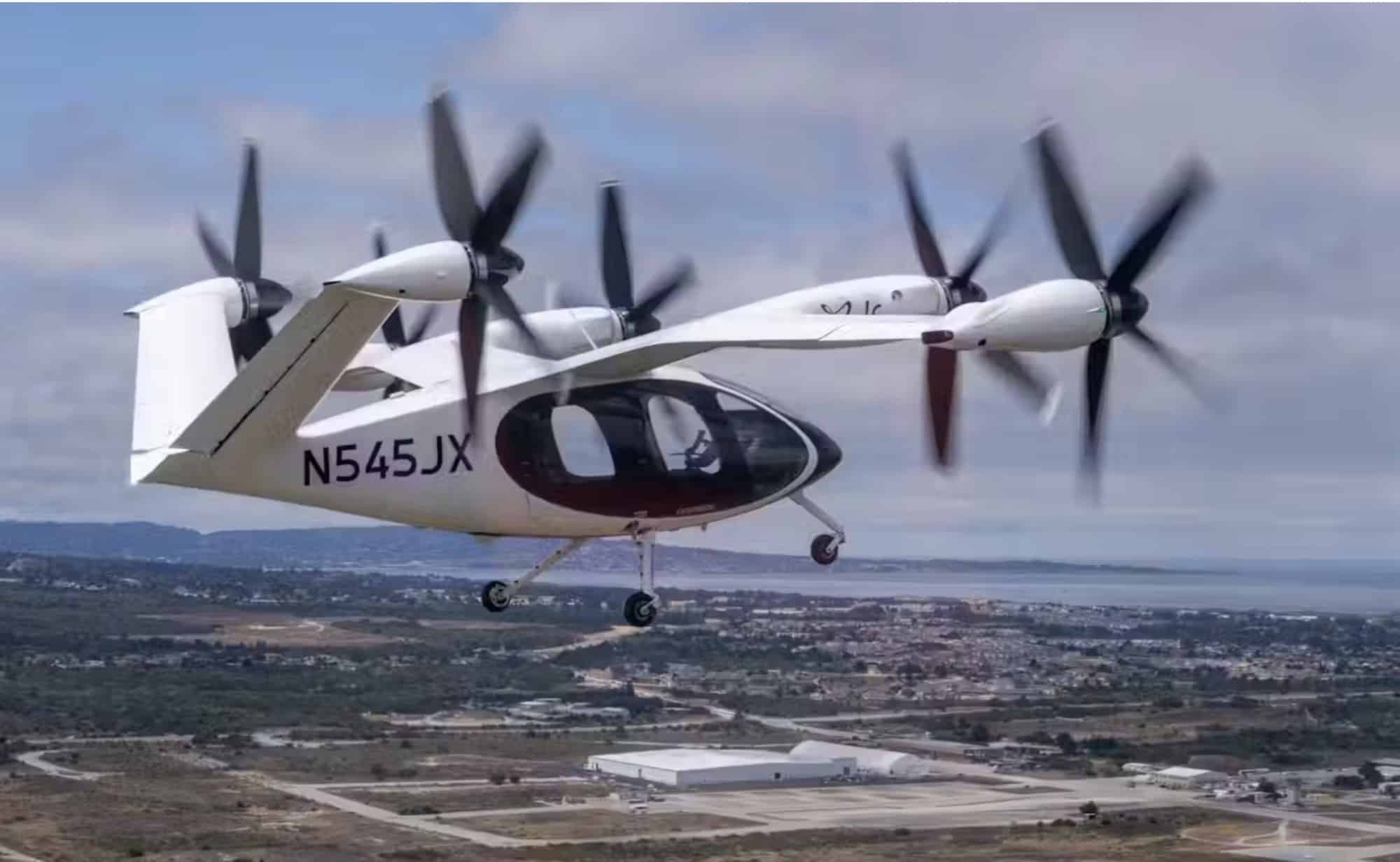 Joby electric aircraft registered N545JX flies in cruise above an airfield.