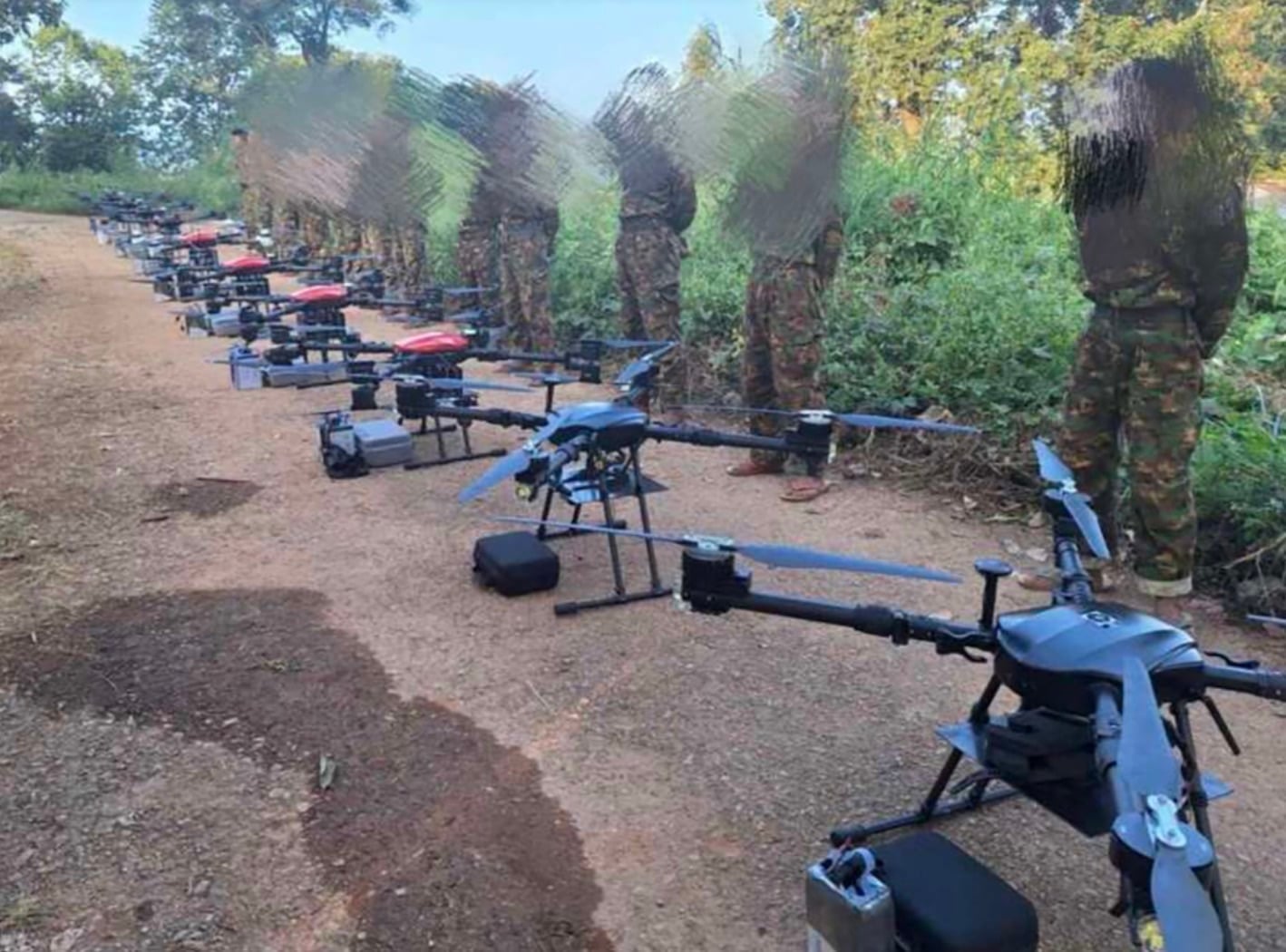 Camouflaged troops stand behind a long row of large blue multirotor drones.