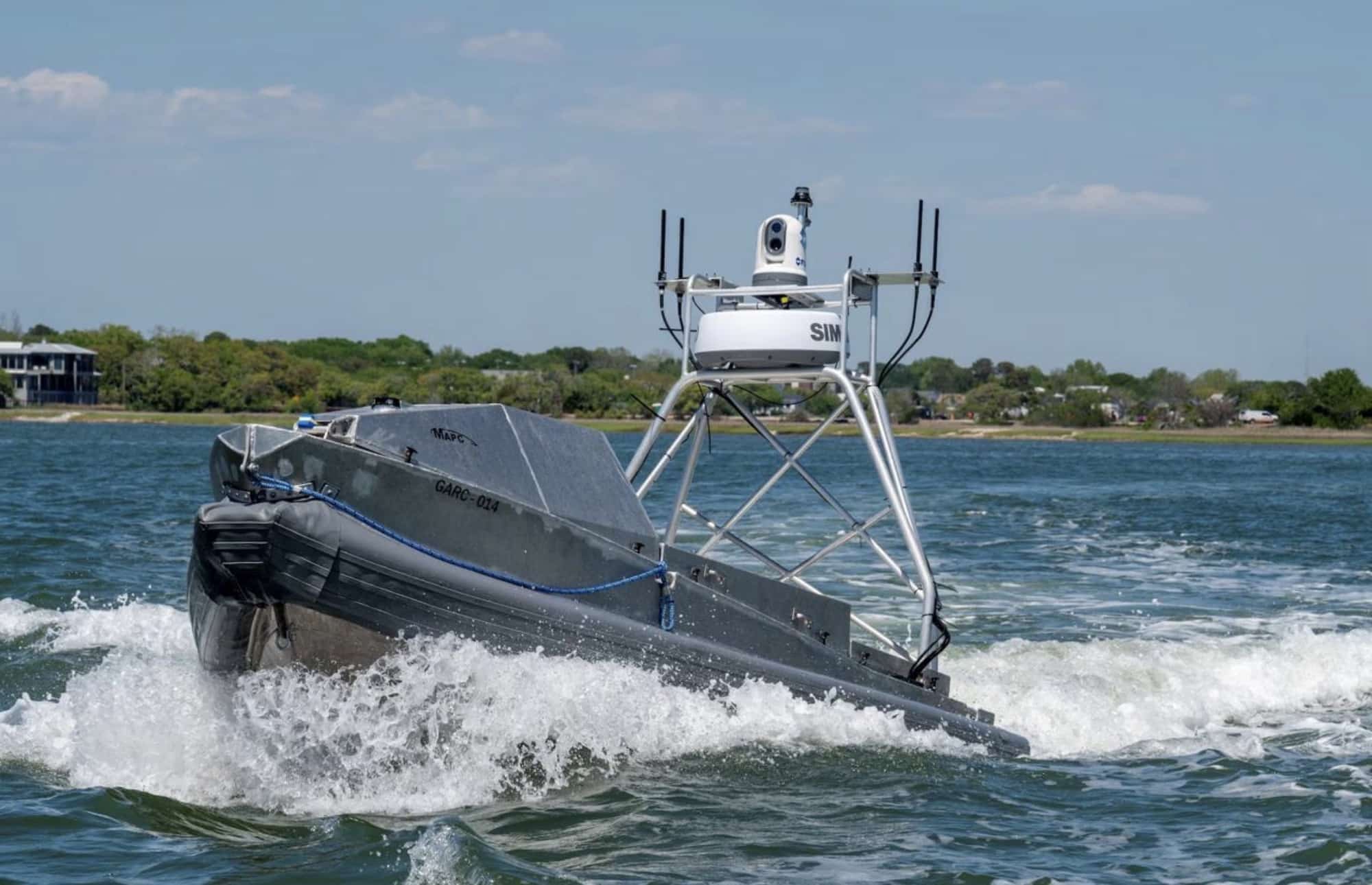 Uncrewed surface vessel running at speed with a sensor mast above the hull.