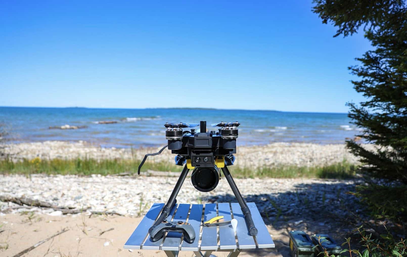 A fiber-optic quadcopter with its cable spool sits on a folding table by a beach.